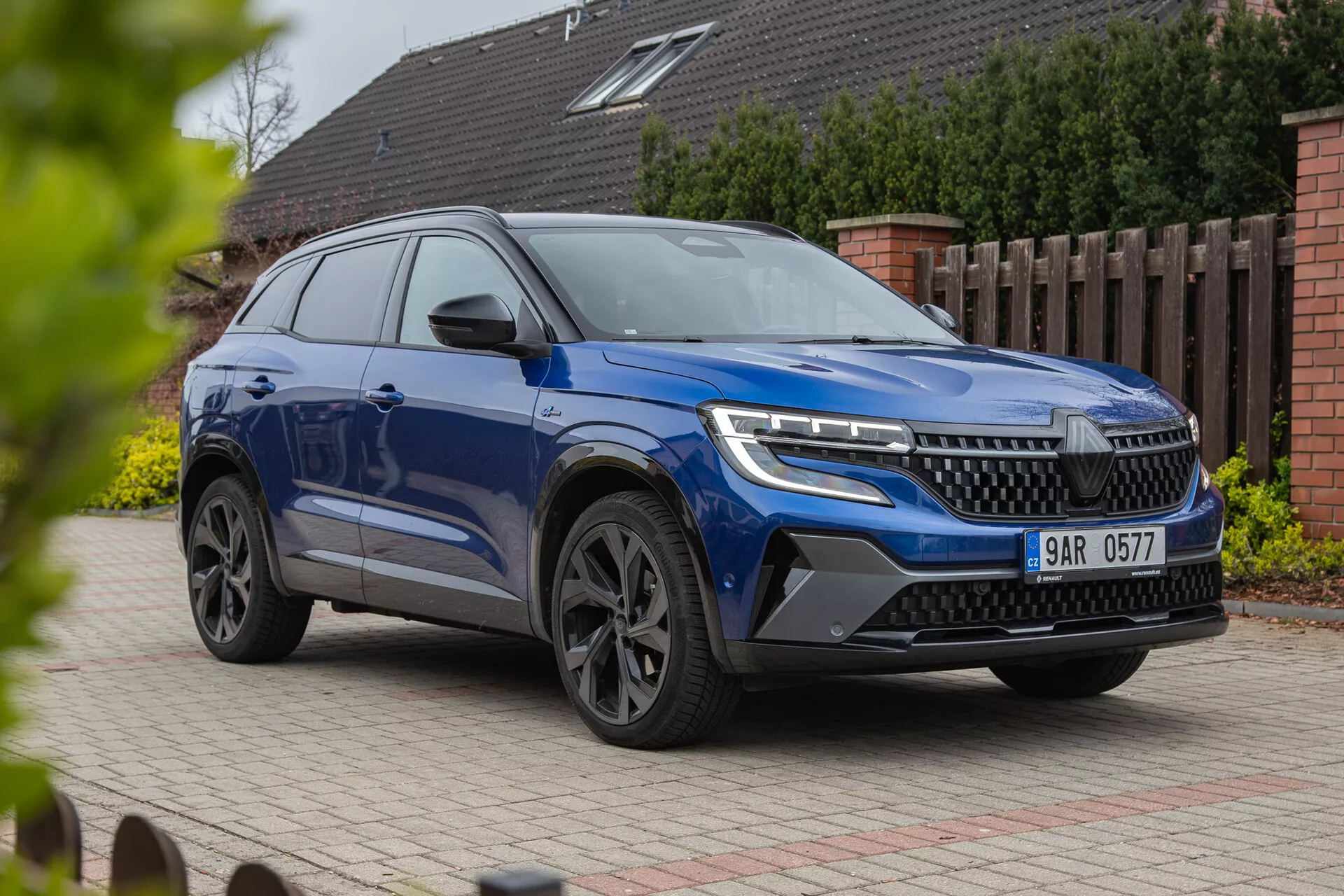 SUV moderno Renault Austral 2022 exibido em perspectiva frontal de três quartos destacando faróis LED, grade proeminente, rodas de liga elegantes e carroceria dinâmica com acabamento de pintura metálica, fotografado de um ângulo baixo para enfatizar sua estatura e características de design contra um fundo residencial.