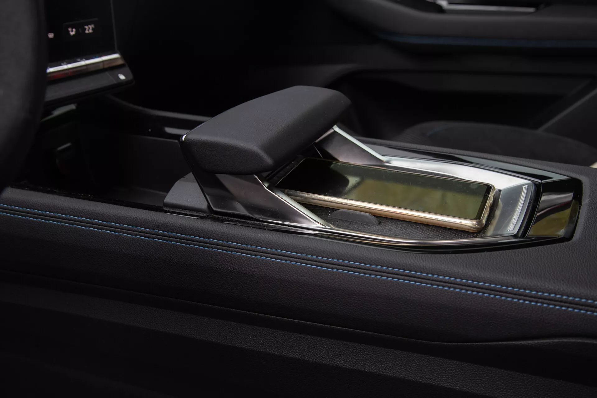 Vista detalhada do console central luxuoso do Renault Austral 2022 com uma alavanca de câmbio automática moderna, apresentando um design ergonômico com detalhes em couro e cromo, contra um acabamento preto brilhante e uma interface de controle de infotenimento sofisticada.