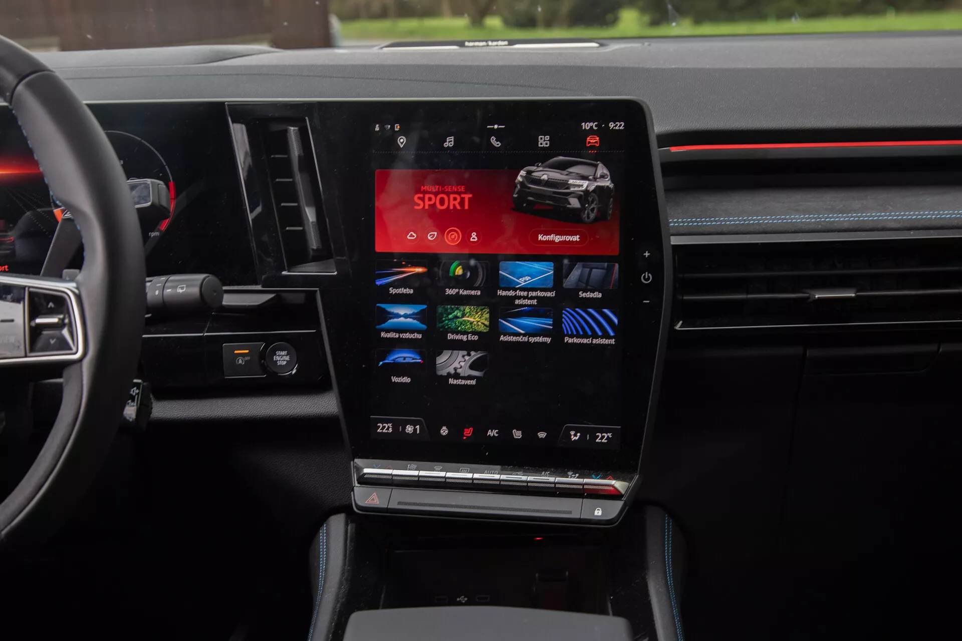 Vista do interior do Renault Austral 2022 destacando o console central com uma grande tela touchscreen vertical apresentando modos de condução como SPORT, Comfort, Eco, junto com configurações de controle climático de duas zonas e controles multifuncionais no volante, encapsulando a essência da tecnologia automotiva moderna e design de luxo.