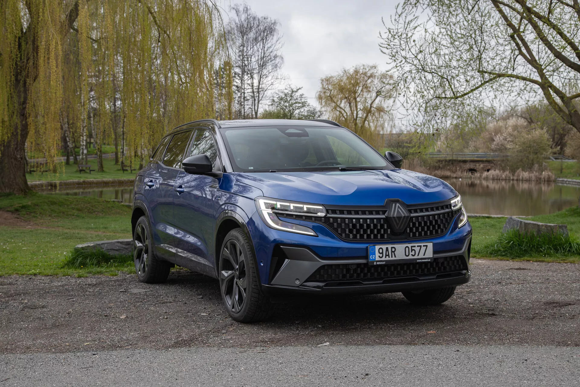 SUV azul Renault Austral 2022 estacionado ao ar livre mostrando a fachada frontal e o lado do motorista com faróis LED, para-choque esportivo e rodas de liga leve contra um plano de fundo natural