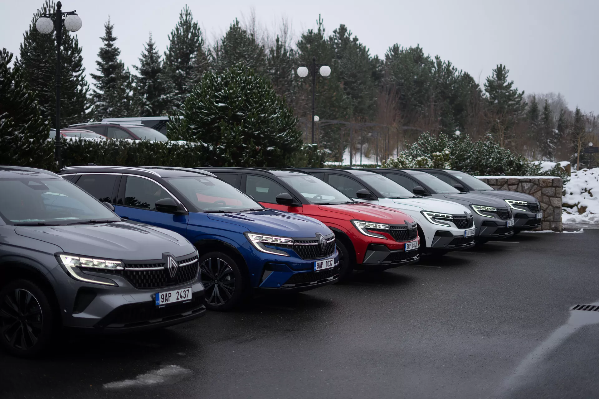 Linha de cinco carros Renault Austral 2022 estacionados a um ângulo de 45 graus em um parque de estacionamento de inverno, mostrando modelos em cinza escuro, azul, vermelho, prata e cinza, com faróis de LED e grades frontais modernas