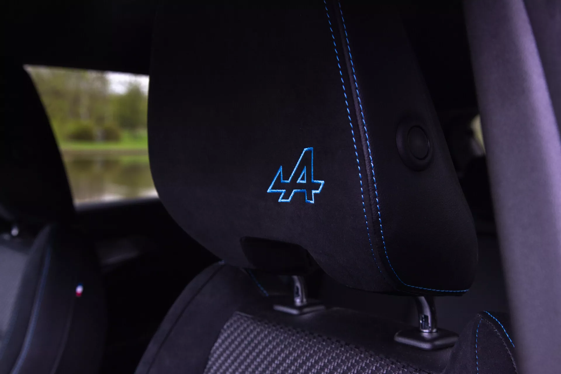 Visão detalhada do interior do Renault Austral 2022 mostrando o assento do motorista de tecido preto com costura azul distintiva e logotipo 'A' estilizado no encosto de cabeça, guia integrado para cinto de segurança visível, sugerindo características de veículo moderno e possivelmente esportivo.