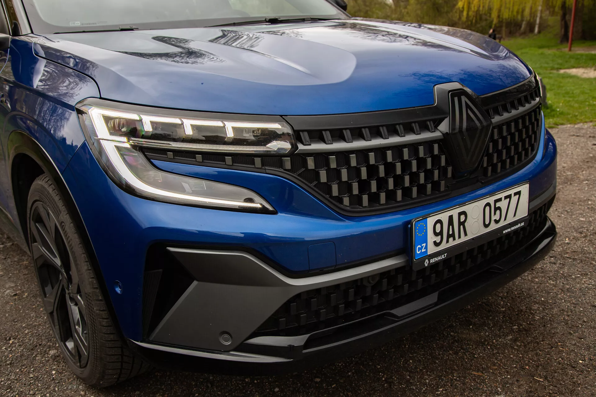 Vista detalhada do Renault Austral 2022, destacando faróis LED elegantes, um design dinâmico da grade e estilo detalhado do para-choque dianteiro e roda, enfatizando a estética e tecnologia modernas do veículo.