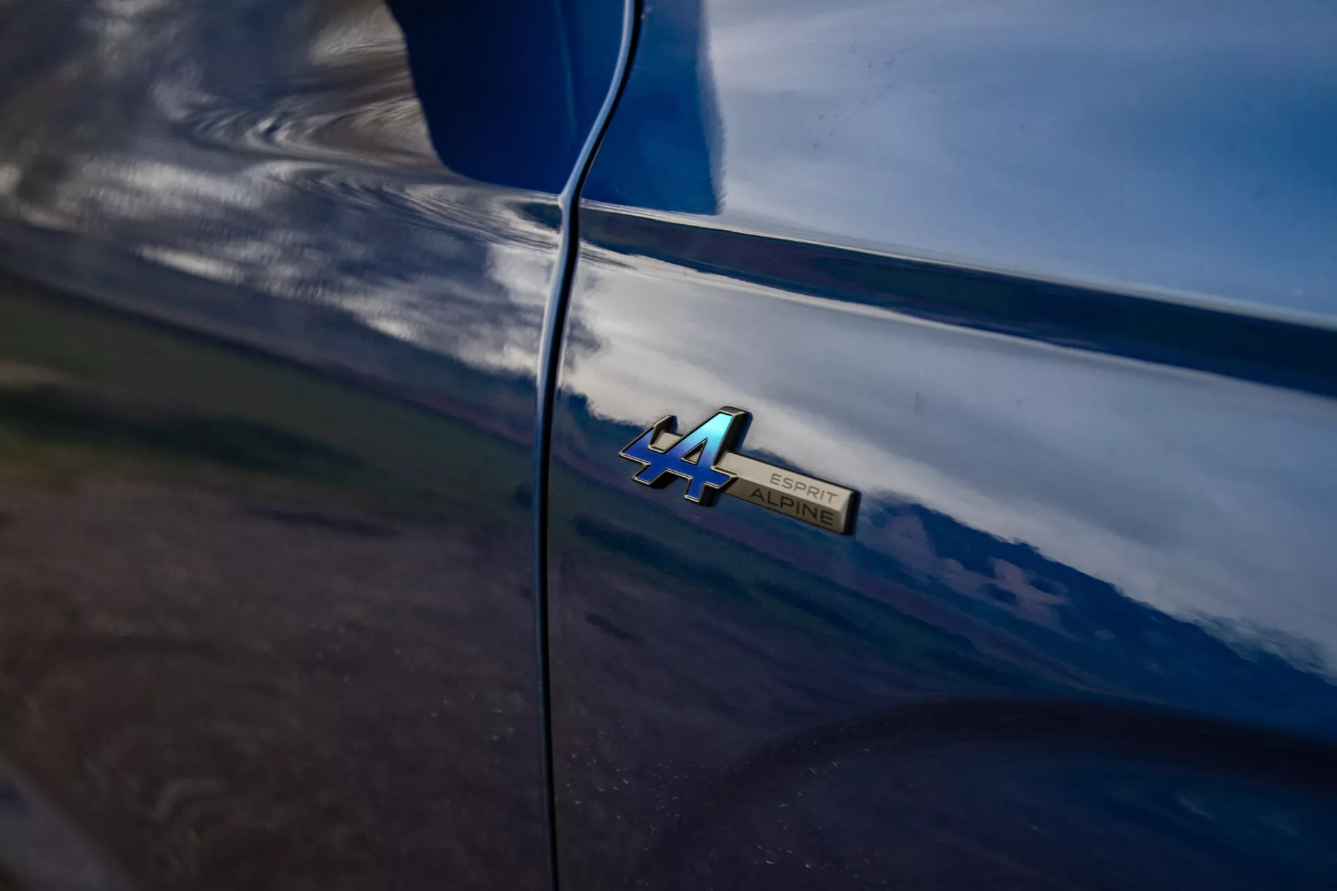 Detalhe em close-up do emblema '4A' do Renault Austral 2022 em carroceria brilhante do carro com reflexos naturais e linhas suaves sugerindo manutenção de alta qualidade e ambiente