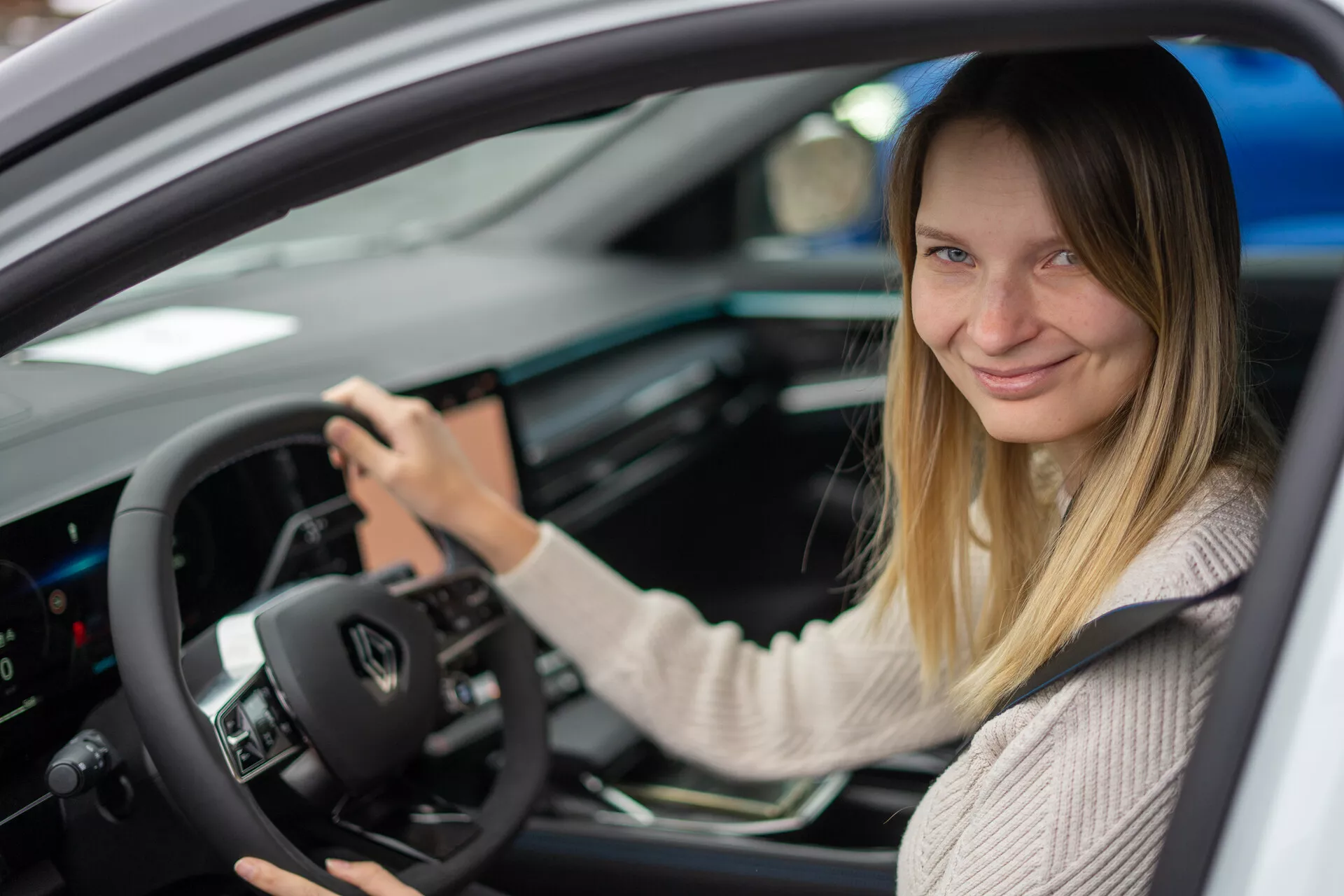 Vista interior do Renault Austral 2022 focada no lado do motorista com uma mulher no assento do motorista, apresentando controles montados no volante, cluster de instrumentos digital e console central com interface touchscreen.