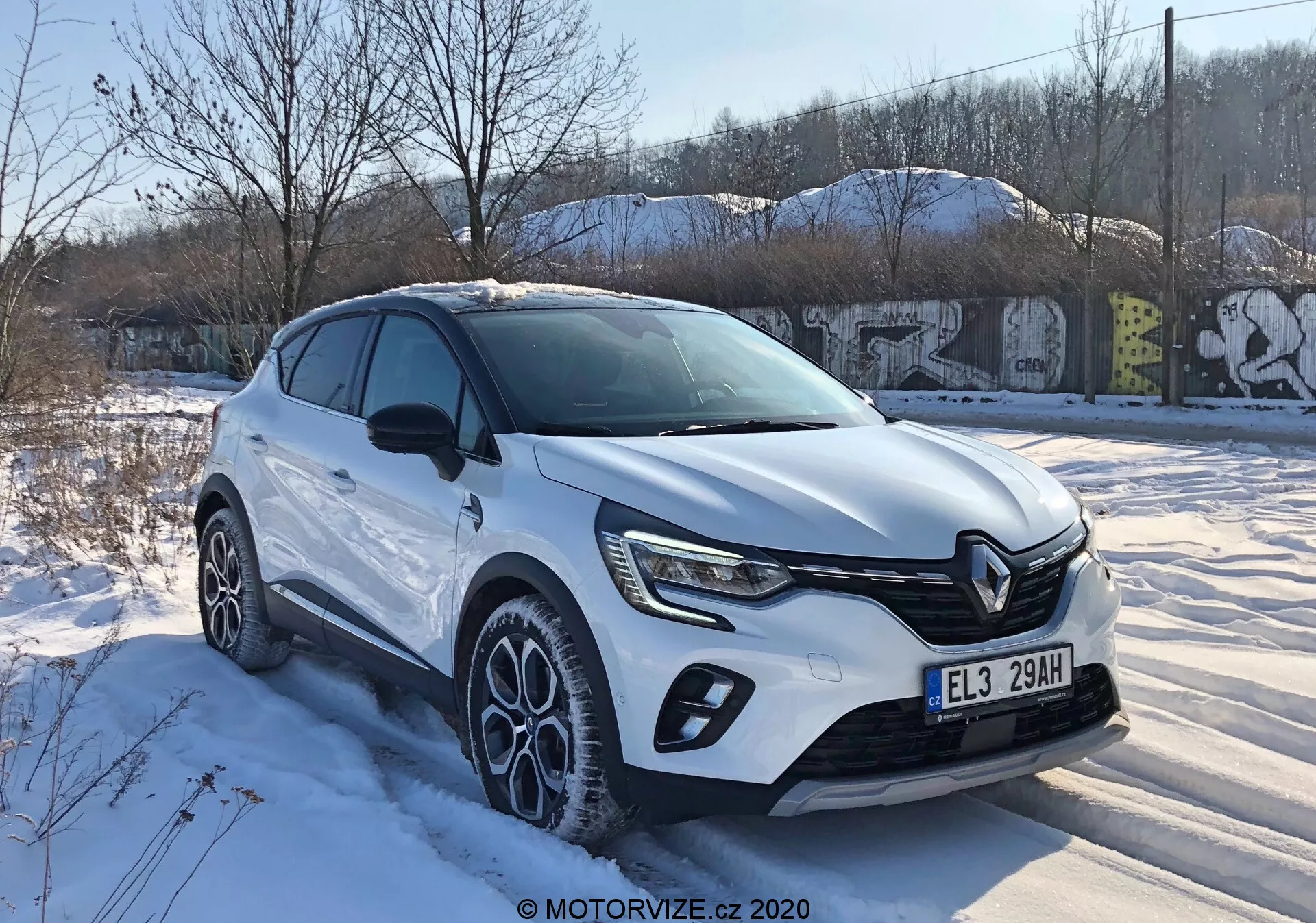 Renault Captur 2020 em vista de três quartos dianteira mostrando design moderno de crossover com grade frontal distinta, faróis LED afiados, revestimento do corpo, grandes rodas de liga leve multifuncionais e cor de carroceria branca sob condições invernais nevadas em um ambiente urbano.