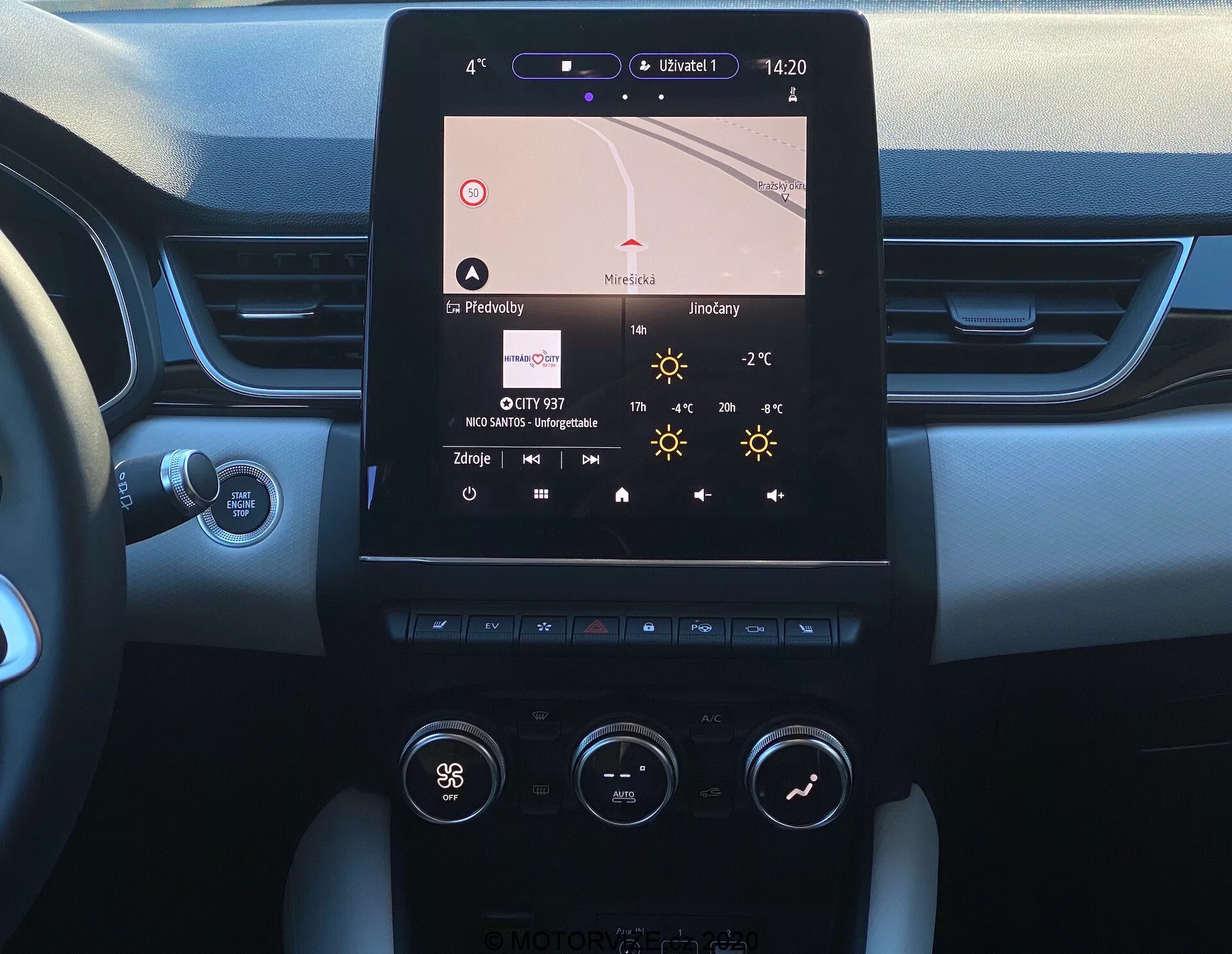 A imagem mostra o console central de um Renault Captur 2020, visto do assento do motorista. O recurso central é uma tela de infotainment touch vertical que exibe navegação, hora (14:20), temperatura (27°C) e detalhes do rádio. Abaixo, o sistema de controle de clima dual-zone com botões e controles é visível, indicando configurações como 'Hi' para a temperatura do lado do motorista. O console combina materiais metálicos e plásticos ao redor da tela e dos controles. As bordas do painel revelam um design de duas tonalidades e toque suave, e um botão Start/Stop é parcialmente visível. A coluna de direção com alavanca de controle é vista, provavelmente para sinais de giro ou outras funções.