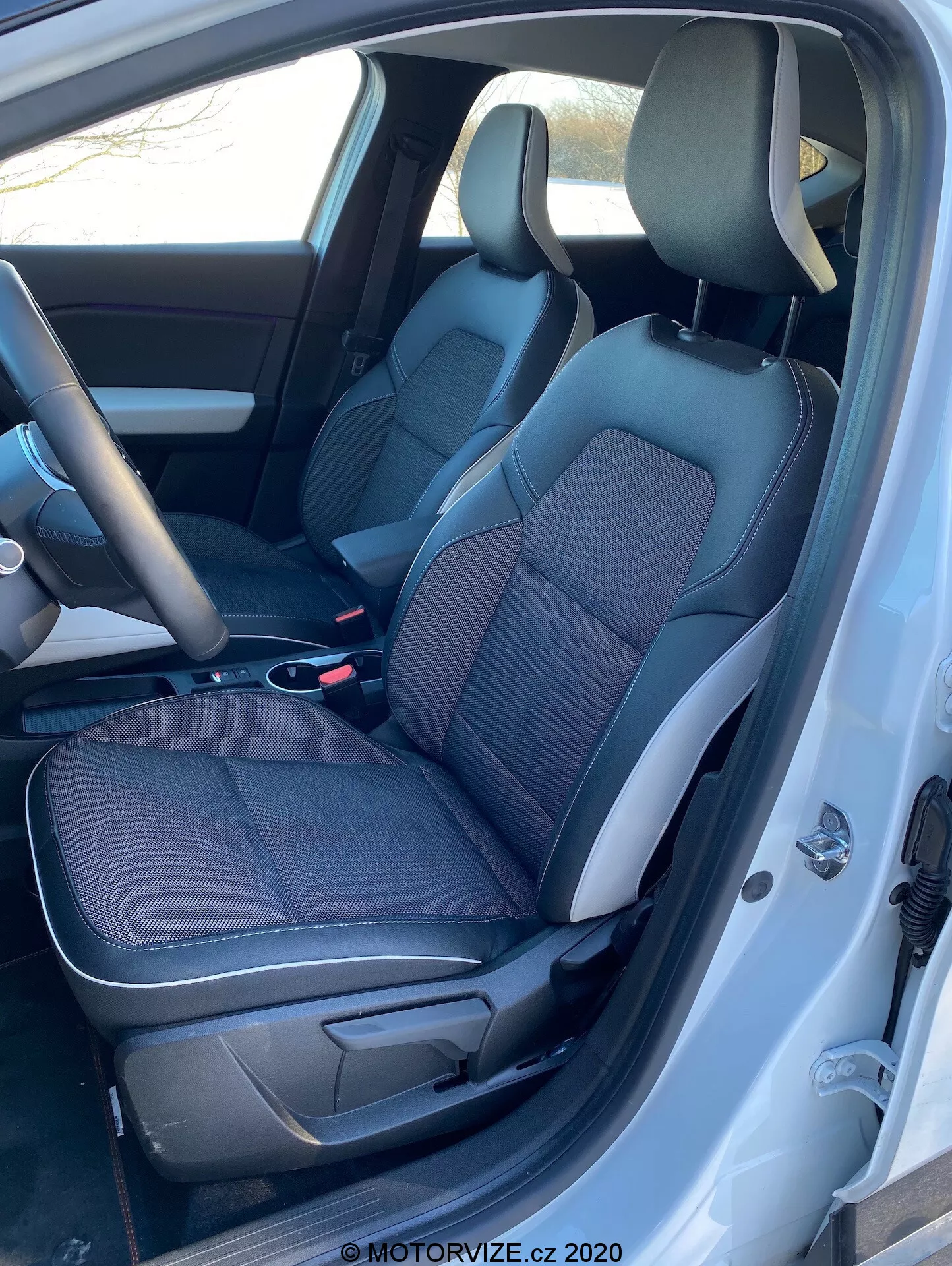 Vista interior do Renault Captur 2020 da área dianteira da cabine, do lado esquerdo, com a porta do motorista aberta, mostrando assentos de tecido e couro preto e cinza, console central, volante e parte do painel.