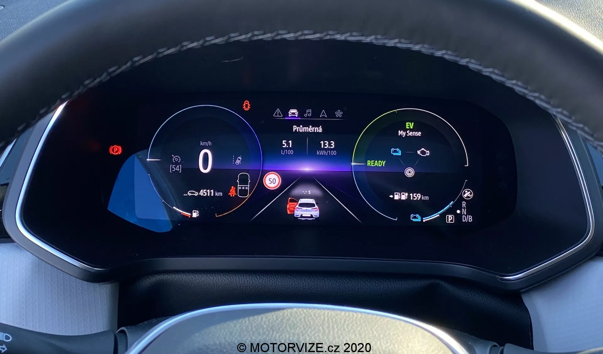 Vista aproximada do painel de instrumentos digital do moderno Renault Captur 2020 a partir da perspectiva do motorista. O display totalmente digital e colorido de alta resolução, inserido em um painel texturizado com costuras visíveis, mostra um velocímetro de 0 km/h com um limite de velocidade de 50 km/h, um gráfico animado central do carro com alertas de segurança e indicadores de bateria, um conta-giros com ícone de modo ecológico 'My Sense', leituras do hodômetro, temperatura externa, indicador de marcha em 'Park' e ícones para assistência de manutenção de faixa, faróis altos automáticos e controle de cruzeiro adaptativo, tudo em um layout bem organizado que destaca a avançada tecnologia automotiva e o design interior.