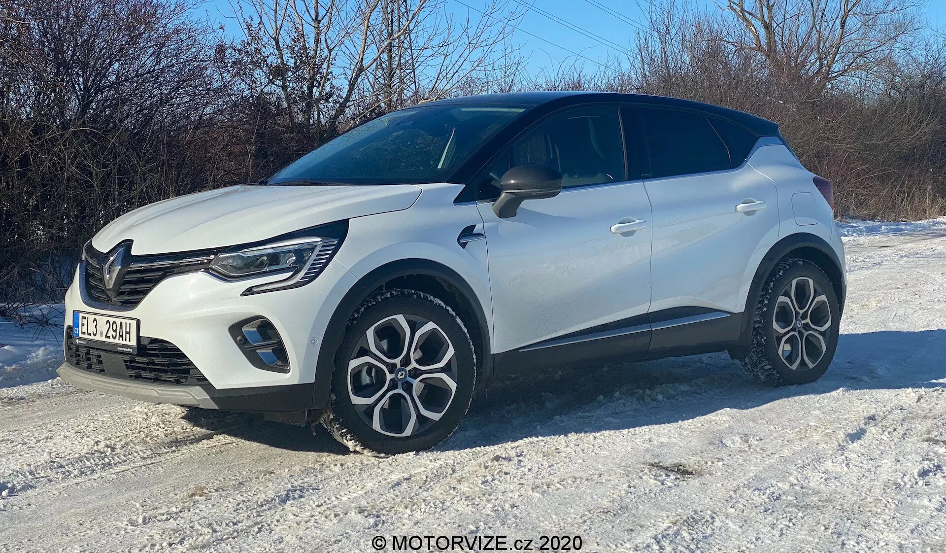 Imagem de um SUV compacto branco em um terreno coberto de neve, capturada em um ângulo frontal de três quartos. O lado direito, capô, grade, faróis LED elegantes, roda dianteira e para-lamas, porta do passageiro e parte da seção traseira são visíveis. O veículo possui design moderno com linhas arrojadas, rodas de liga leve de design distinto com vários raios, carroceria de duas cores com teto preto e padrão de grade distinto com luzes de circulação diurna visíveis.
