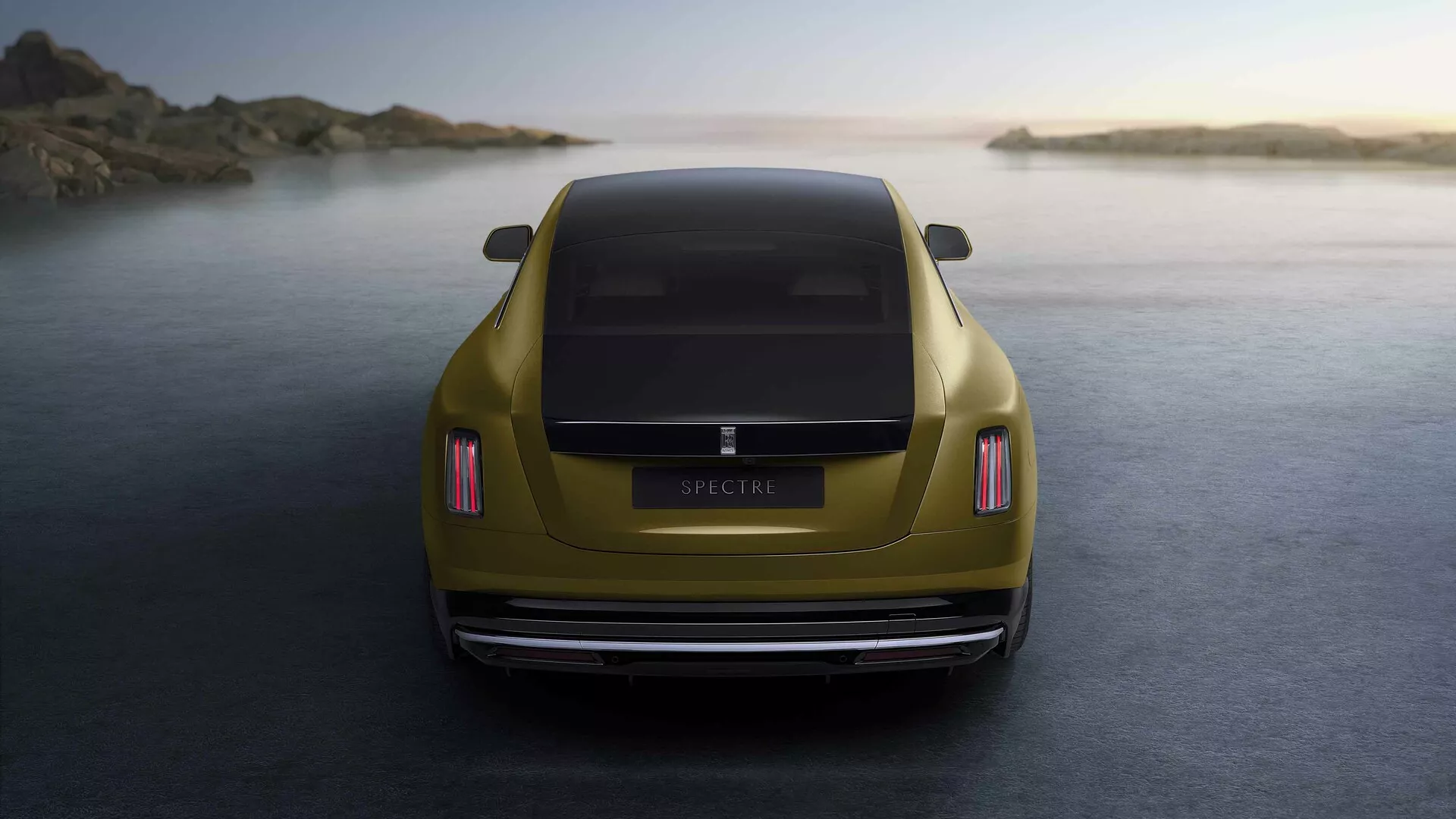 Rolls-Royce Spectre 1ª geração 2023 em dourado metálico capturado de uma perspectiva traseira na hora dourada, destacando suas lanternas traseiras LED, design aerodinâmico do porta-malas, para-choque traseiro polido, sistema de escapamento duplo e posicionado contra um tranquilo pano de fundo costeiro.