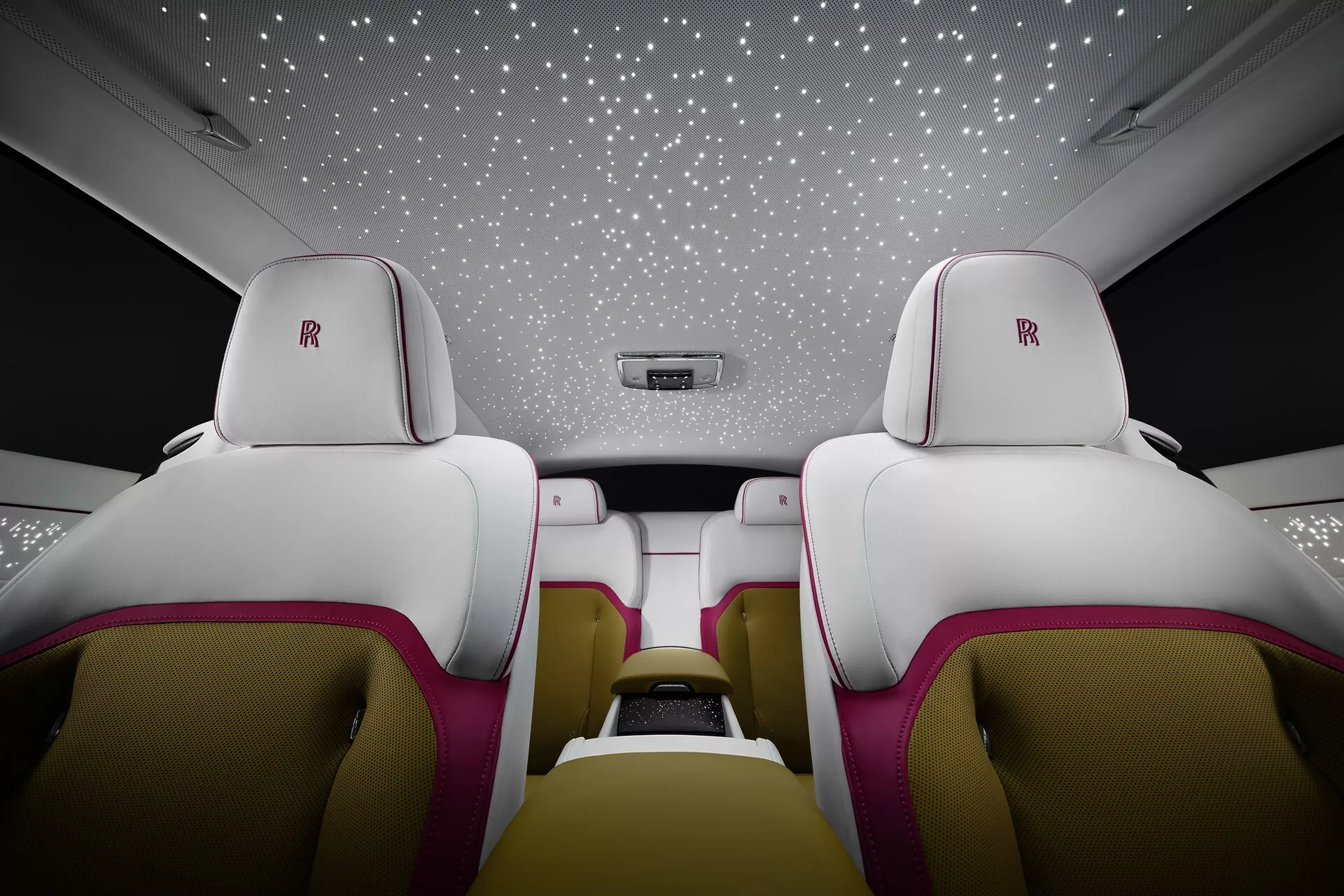 Interior luxuoso do Rolls-Royce Spectre 2023 de primeira geração, bancos traseiros de couro branco com detalhes magenta, logotipo da Rolls-Royce nos encostos de cabeça e teto com luzes simulando um céu estrelado