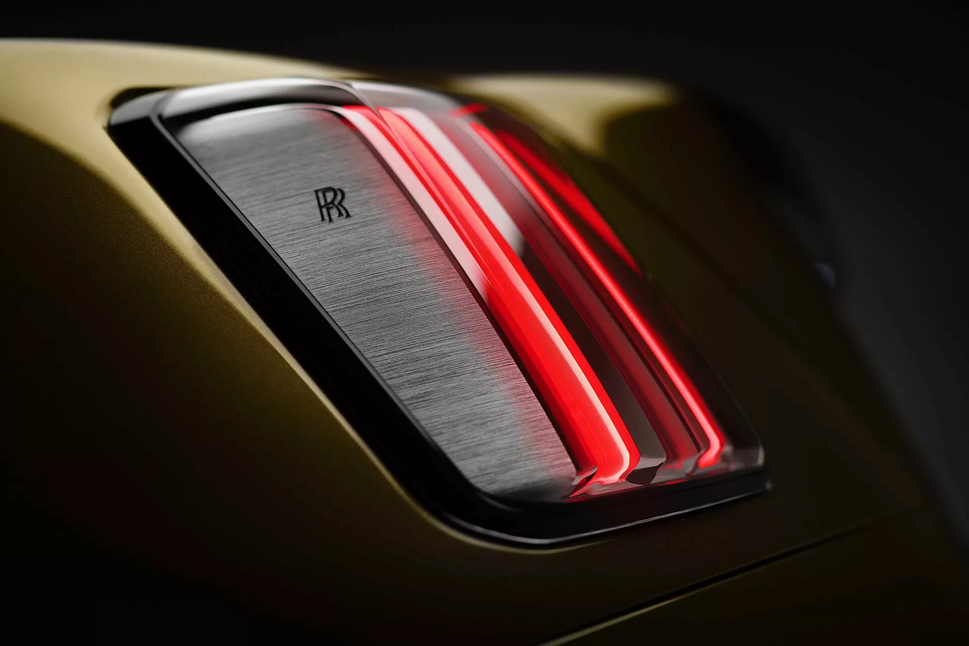 Vista de perto da luz traseira do Rolls-Royce Spectre 2023 destacando o design moderno de LED e o emblemático emblema de duplo 'R' em uma carroçaria cinza metálico