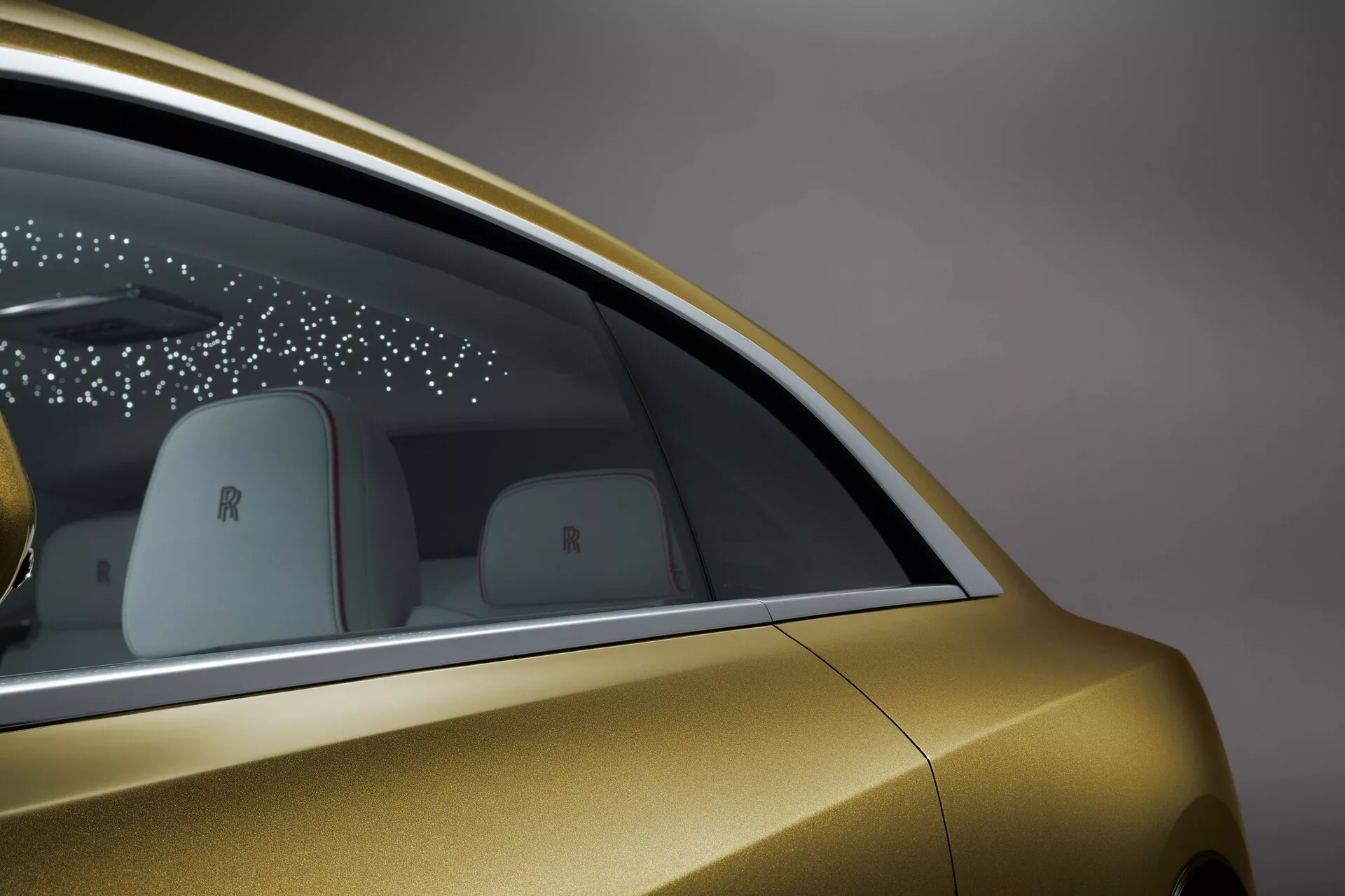 Vista lateral em close-up do Rolls-Royce Spectre 2023, mostrando o acabamento em ouro metálico, design da janela traseira, tecnologia de porta elegante e detalhes de marca de luxo