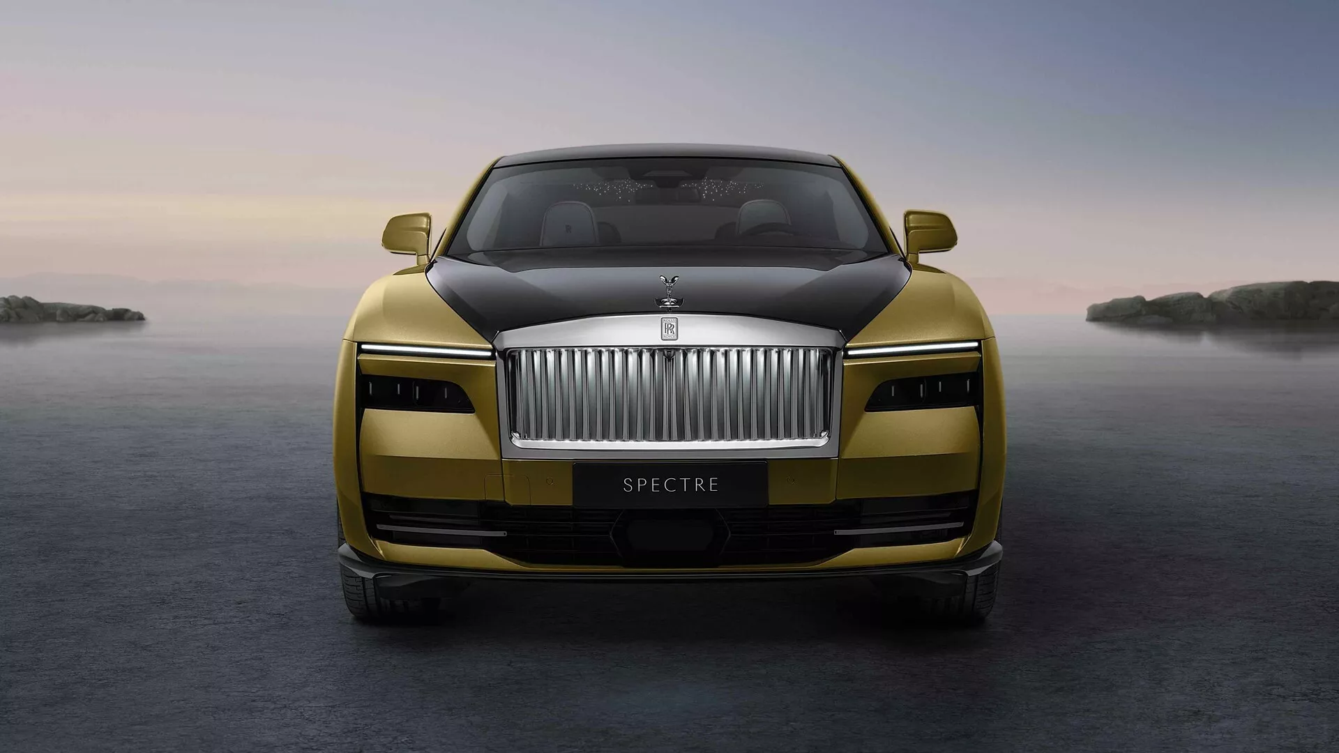 Vista frontal do Rolls-Royce Spectre 2023 mostrando grade proeminente, emblema, faróis LED e acabamento metálico com recursos avançados destacados contra um fundo sereno