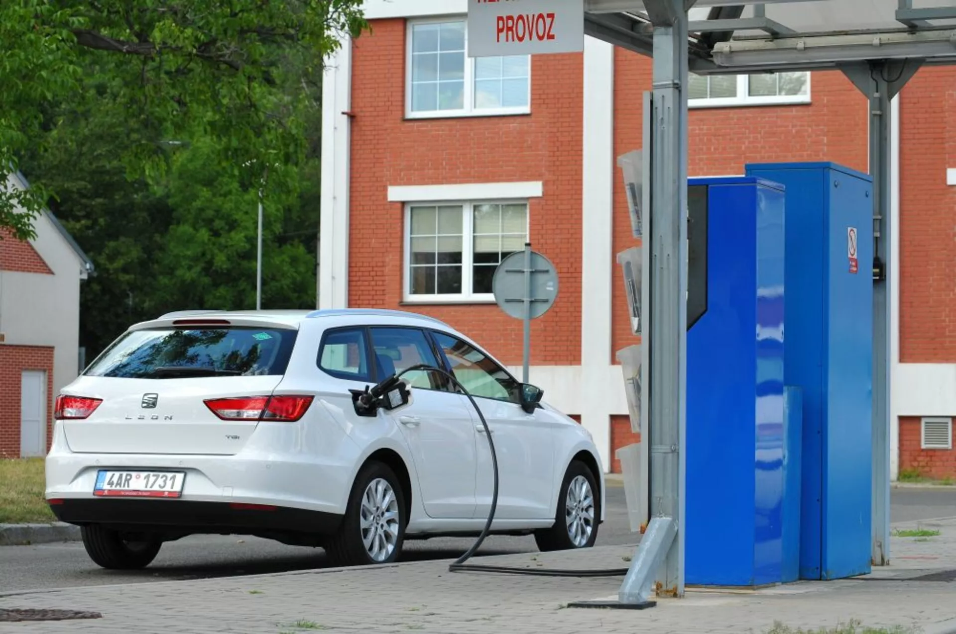 Carro hatchback branco Seat Leon SC 2016, elétrico ou plug-in híbrido, estacionado em uma estação de carregamento de EV, mostrando uma vista traseira de três quartos destacando as luzes traseiras, o vidro traseiro, o perfil da escotilha e a porta de carga no lado direito