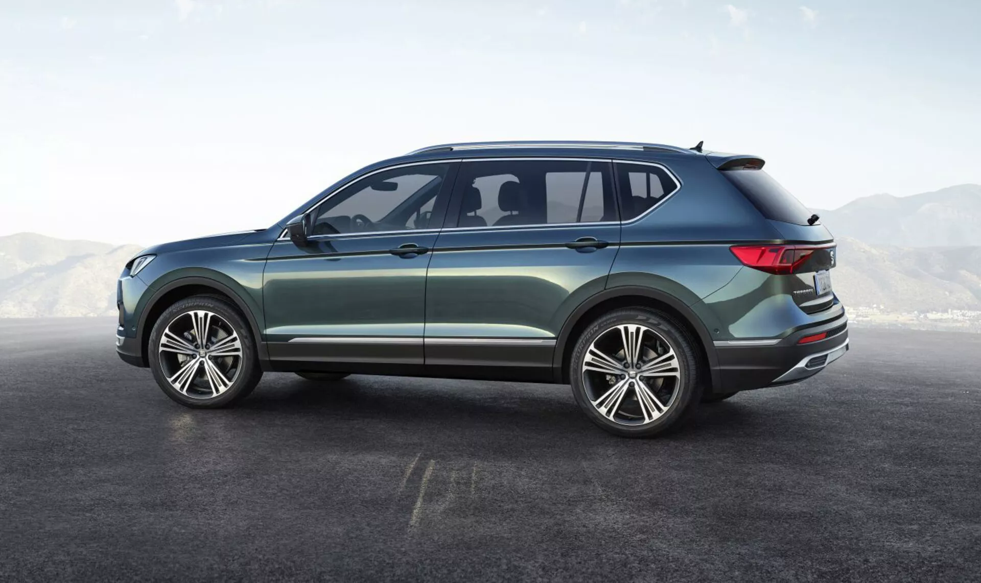 SUV Seat Tarraco 2019 exibindo seu ângulo traseiro lateral, apresentando grandes rodas de liga leve multirraios, design de quatro portas, janelas laterais elegantes com uma pequena janela traseira aerodinâmica, linha do teto suavemente inclinada com spoiler integrado, luzes traseiras LED envolventes, pintura metálica com acabamento exterior cromado, destacando seu design moderno e versátil