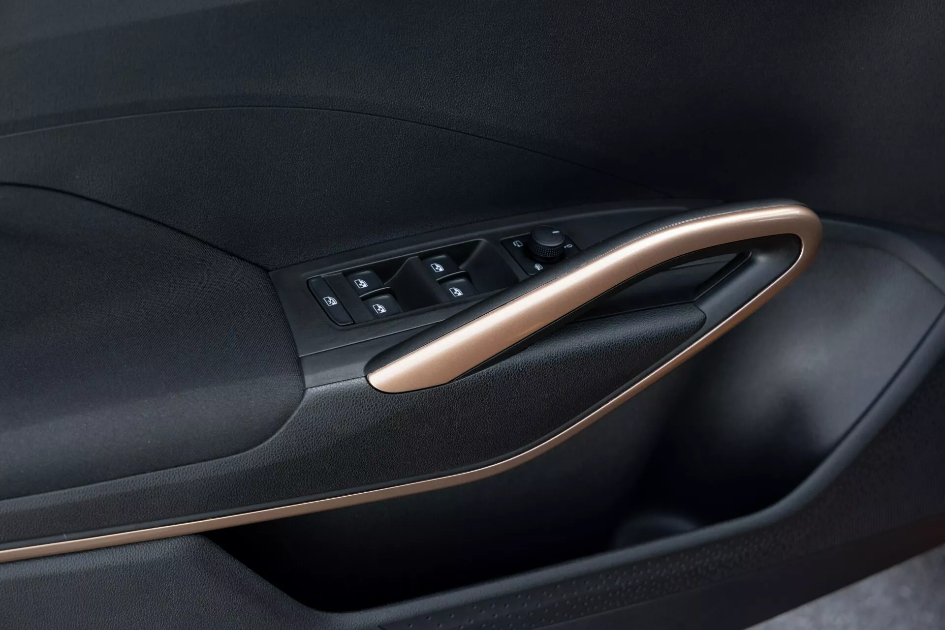 Visão detalhada do painel interno da porta do Skoda Fabia 2021, destacando o módulo de controle da porta. A imagem, tirada de um ângulo oblíquo, ressalta a disposição dos botões e o acabamento da porta. O módulo de controle da porta inclui botões para os controles das janelas, travas das portas e possivelmente ajustes dos espelhos. O painel apresenta um design bicolor com material preto acentuado por acabamentos metálicos ou em madeira, enfatizando o design moderno e ergonômico do carro.