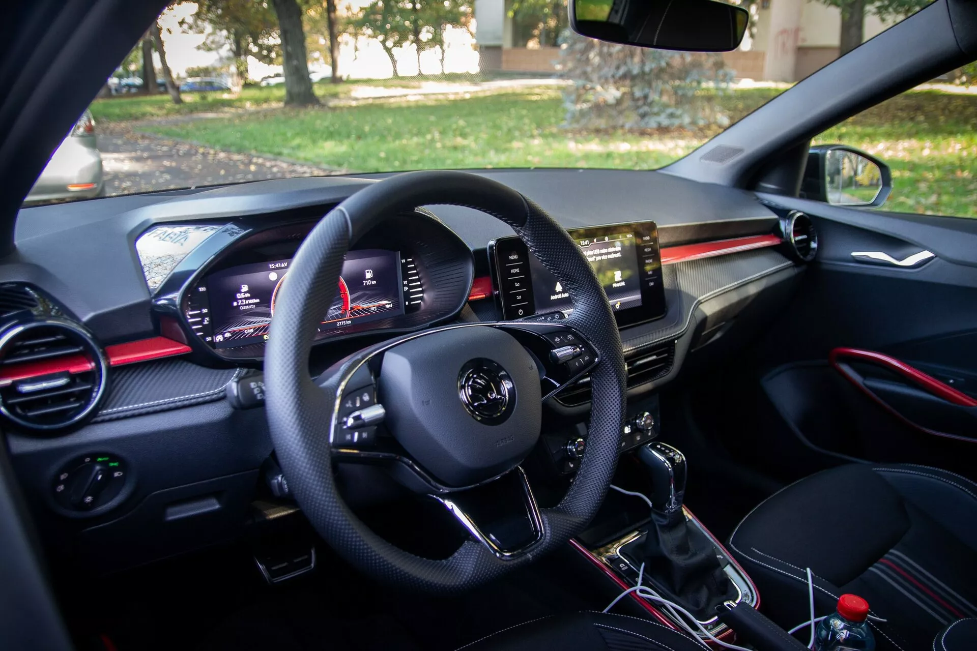 Vista do interior de um moderno Skoda Fabia 2021 a partir da perspetiva do condutor, com painel de controlo na porta do condutor, volante multifuncional, painel de instrumentos digital, saídas de ar com detalhes em vermelho, ecrã tátil central de infoentretenimento, alavanca de mudanças manual e área do assento do passageiro com porta-luvas e saída de ar correspondente.