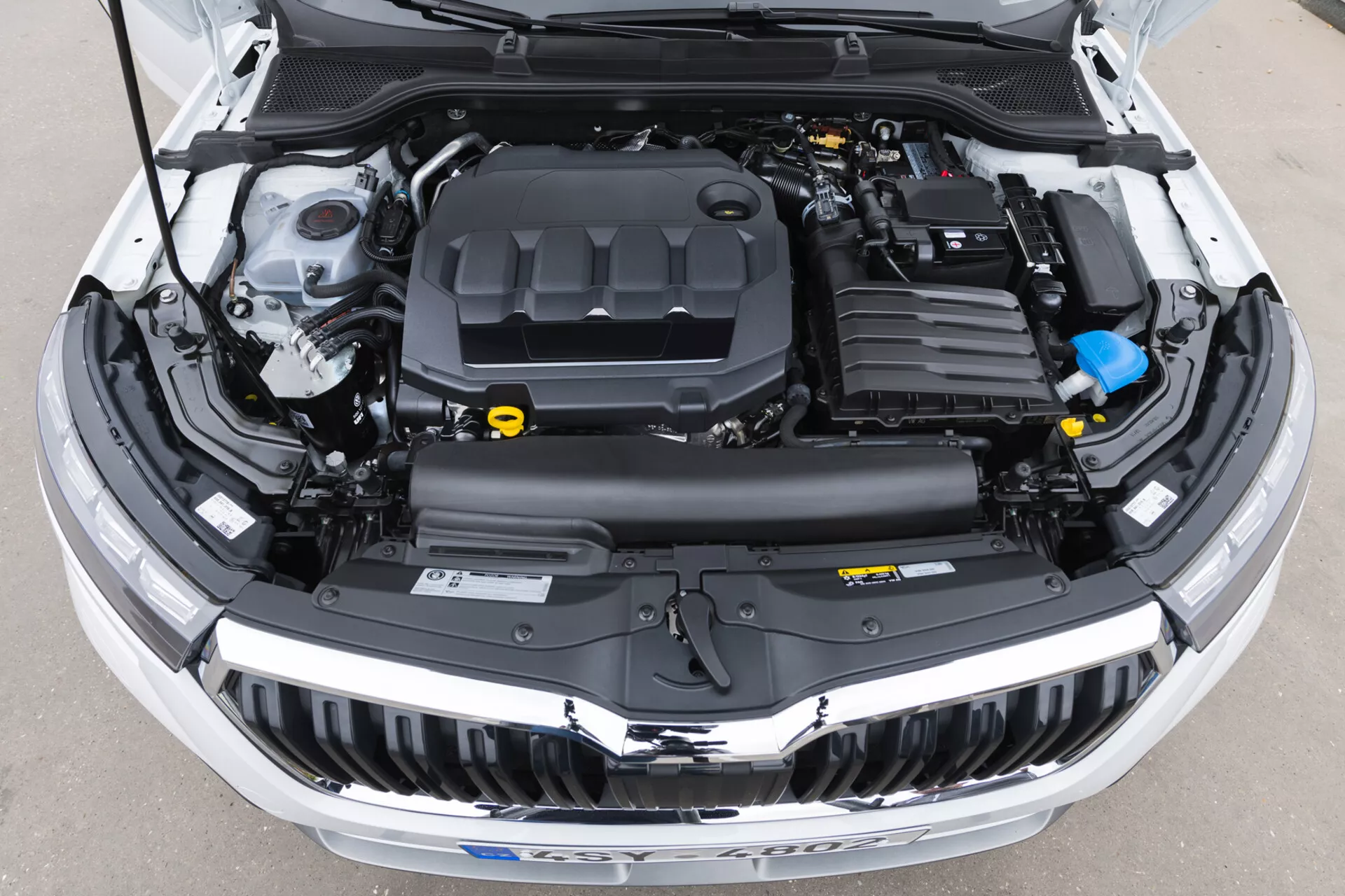 Vista detalhada do compartimento do motor aberto do Skoda Kamiq 2019 mostrando a tampa do motor, coberturas de plástico, reservatórios de fluidos e condutas eletrónicas sem elementos de design exterior visíveis