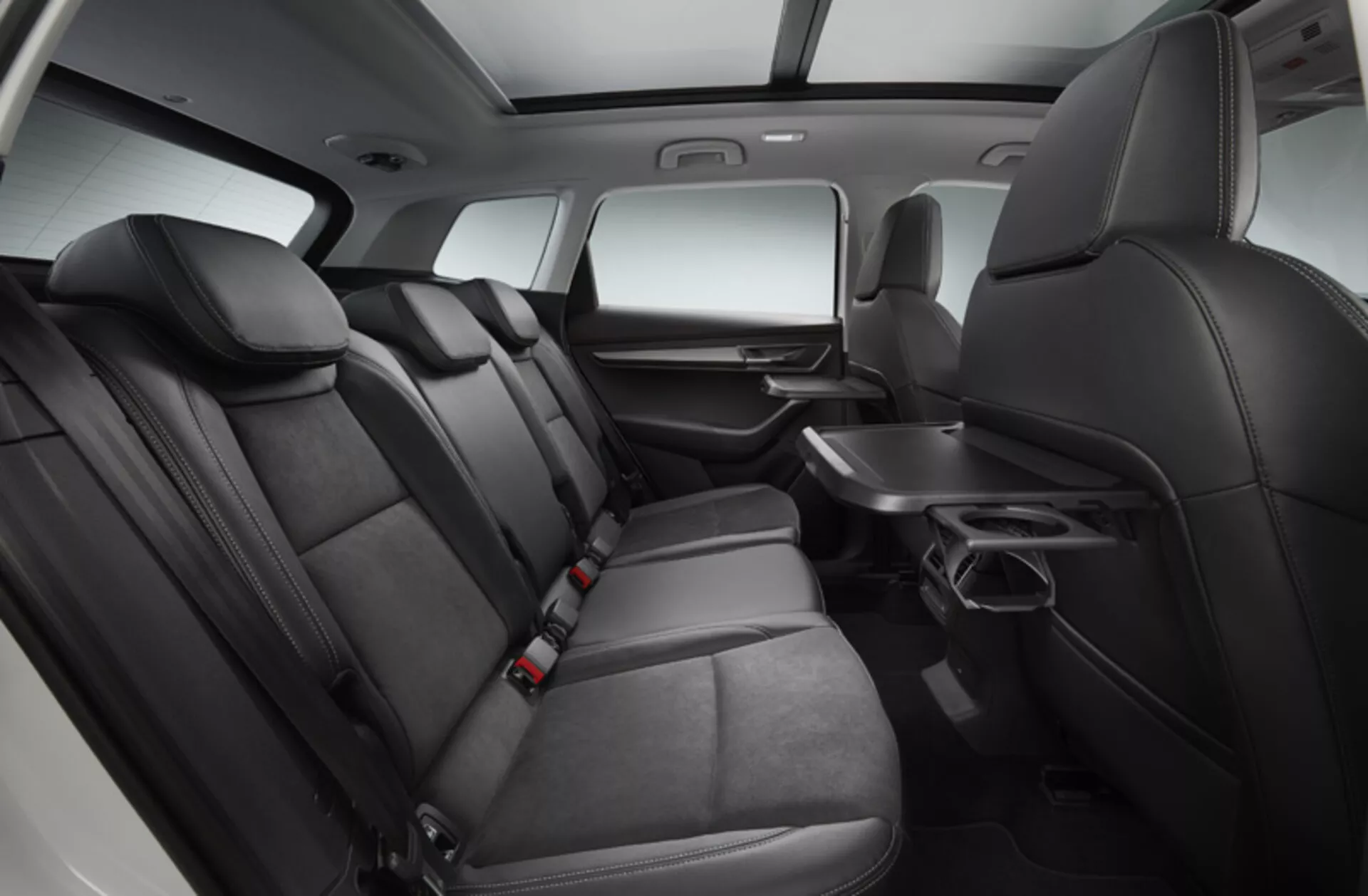 Interior do Skoda Karoq 2017 mostrando uma área de assentos traseiros espaçosa e confortável com estofamento premium em dois tons, controle de clima traseiro, apoio de braço retrátil com porta-copos e sistema de entretenimento