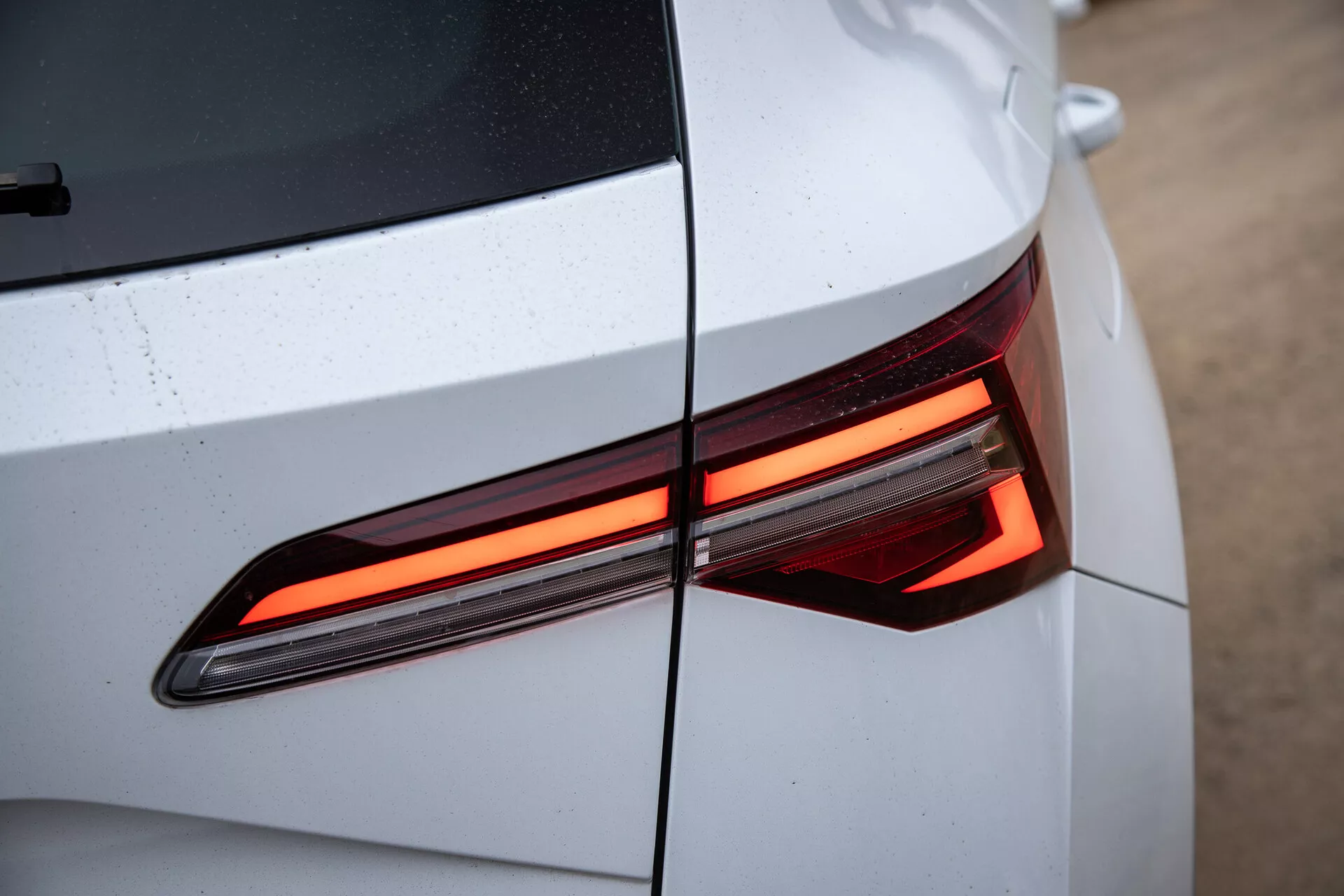 Close-up da seção traseira do Skoda Karoq 2021 mostrando o design moderno da luz traseira LED, com ênfase nas linhas angulares e na carroceria brilhante e de cor clara com gotas de água visíveis