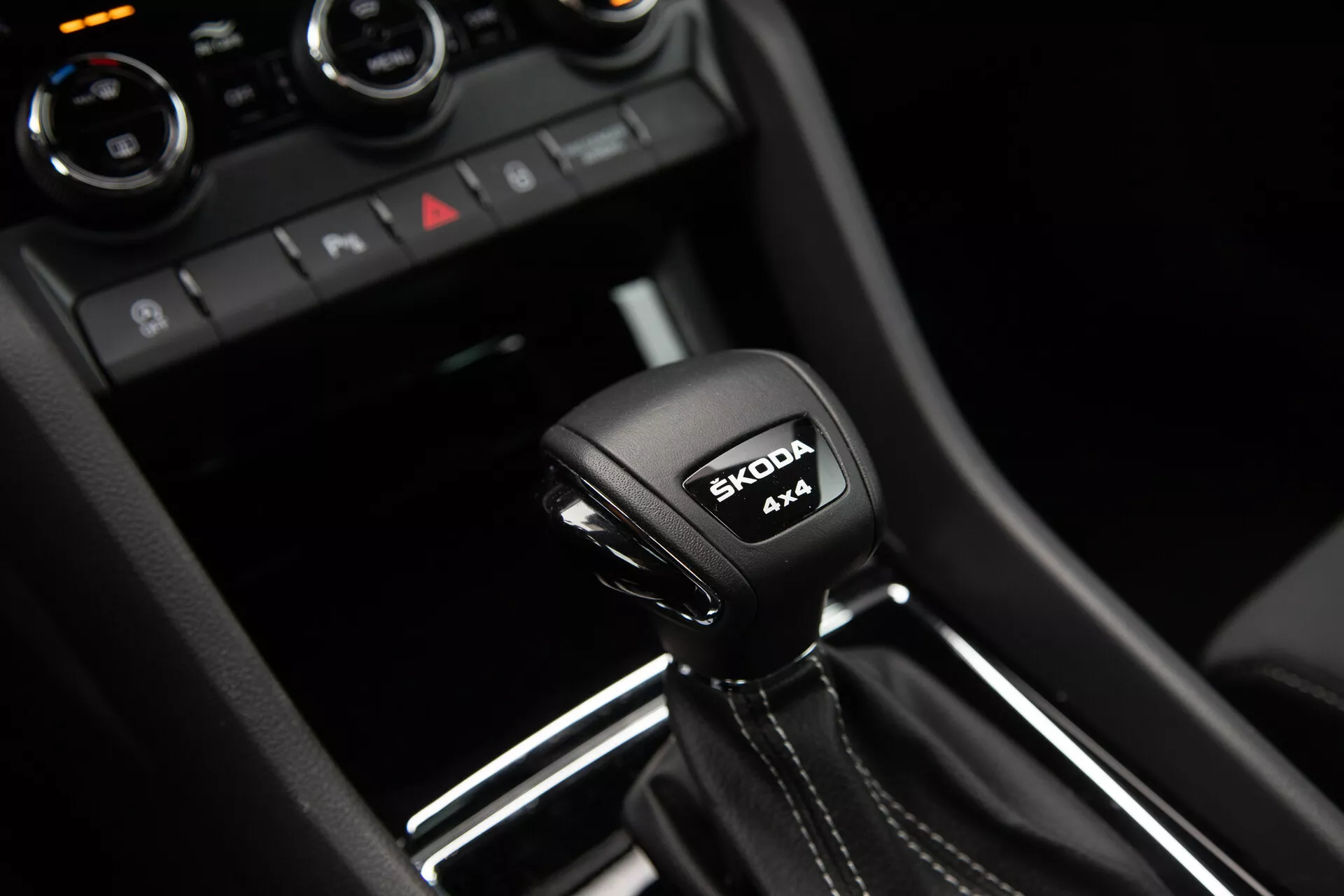 Alavanca de mudanças automática do Škoda Karoq 2021 com inscrição do sistema 4x4 e logotipo da Škoda, rodeada por detalhes interiores modernos em preto brilhante e acabamento metálico.