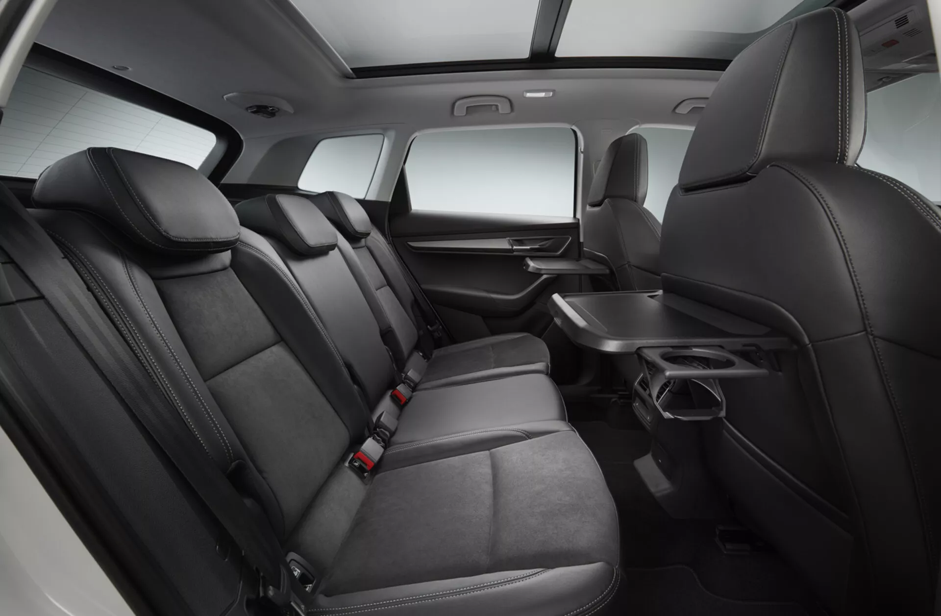 Vista interior de um Skoda Karoq 2017 focada na área de assentos da segunda fila com assentos de couro preto premium, apoio de braço reclinável com porta-copos, painel de porta com controles elétricos, bolsos de armazenamento atrás dos assentos da primeira fila, cintos de segurança para todas as posições, e um console central que se estende até a segunda fila, tudo sob iluminação de estúdio realçada
