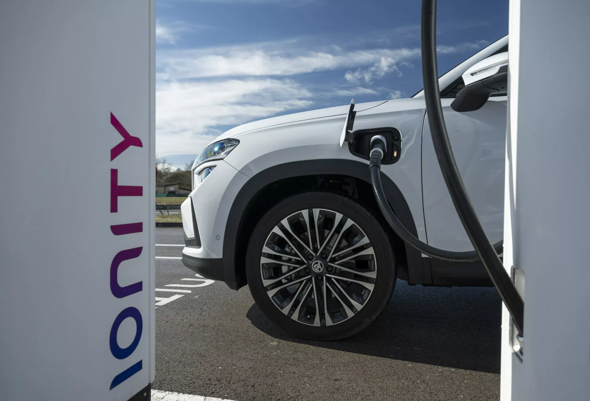 Vista lateral de perto de um veículo elétrico Skoda Kodiaq branco 2024 carregando em uma estação Ionity, exibindo tecnologia de carga rápida e design moderno