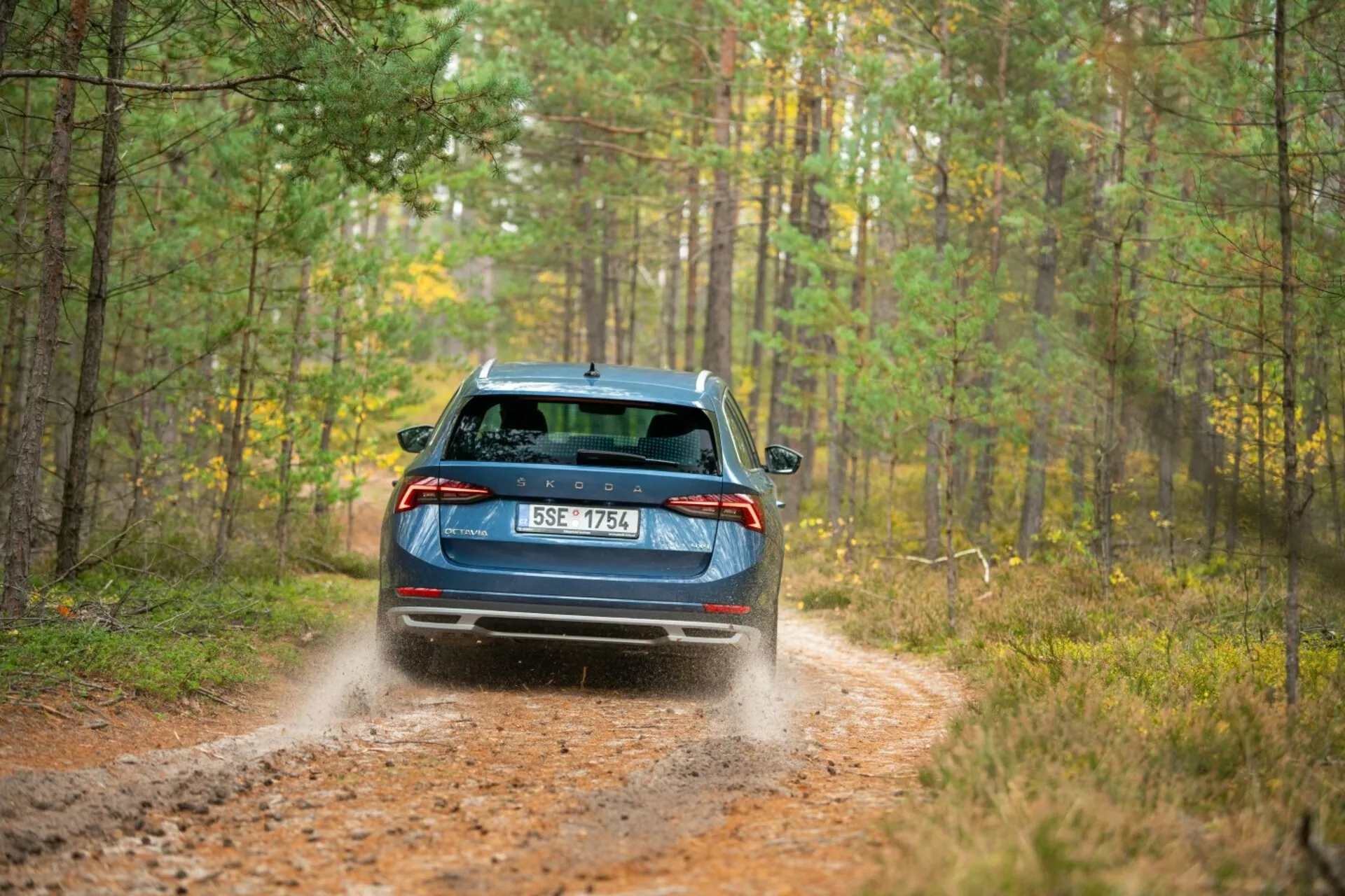 Limusine Skoda Octavia 2017 azul, exibindo lanternas traseiras LED, limpador do vidro traseiro e escapamento duplo em uma trilha florestal com deslocamento dinâmico de terra indicando capacidades de tração integral