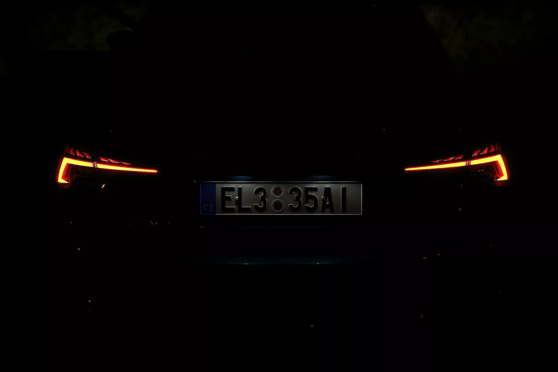 Vista traseira de um Skoda Octavia 2020 Limousine, fotografado à noite ou em um ambiente com pouca luz. A imagem se concentra nas luzes traseiras iluminadas e na placa de licença, mostrando um design moderno e angular. Os detalhes do carro estão obscurecidos devido à baixa iluminação, destacando a seção traseira elegante e contemporânea.