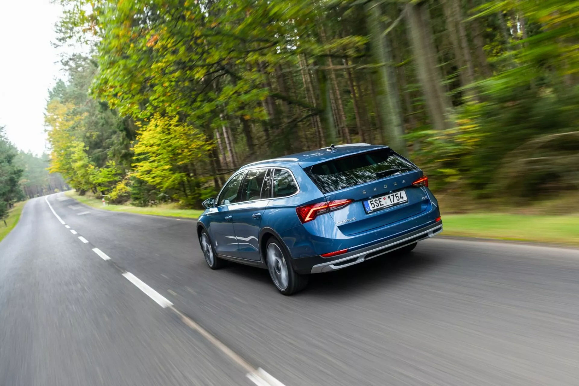 Skoda Octavia carrinha de 2017 em movimento, captada a partir de um ângulo traseiro de três quartos a destacar o design aerodinâmico, a mala traseira hatchback e as luzes traseiras horizontais numa estrada ladeada por floresta