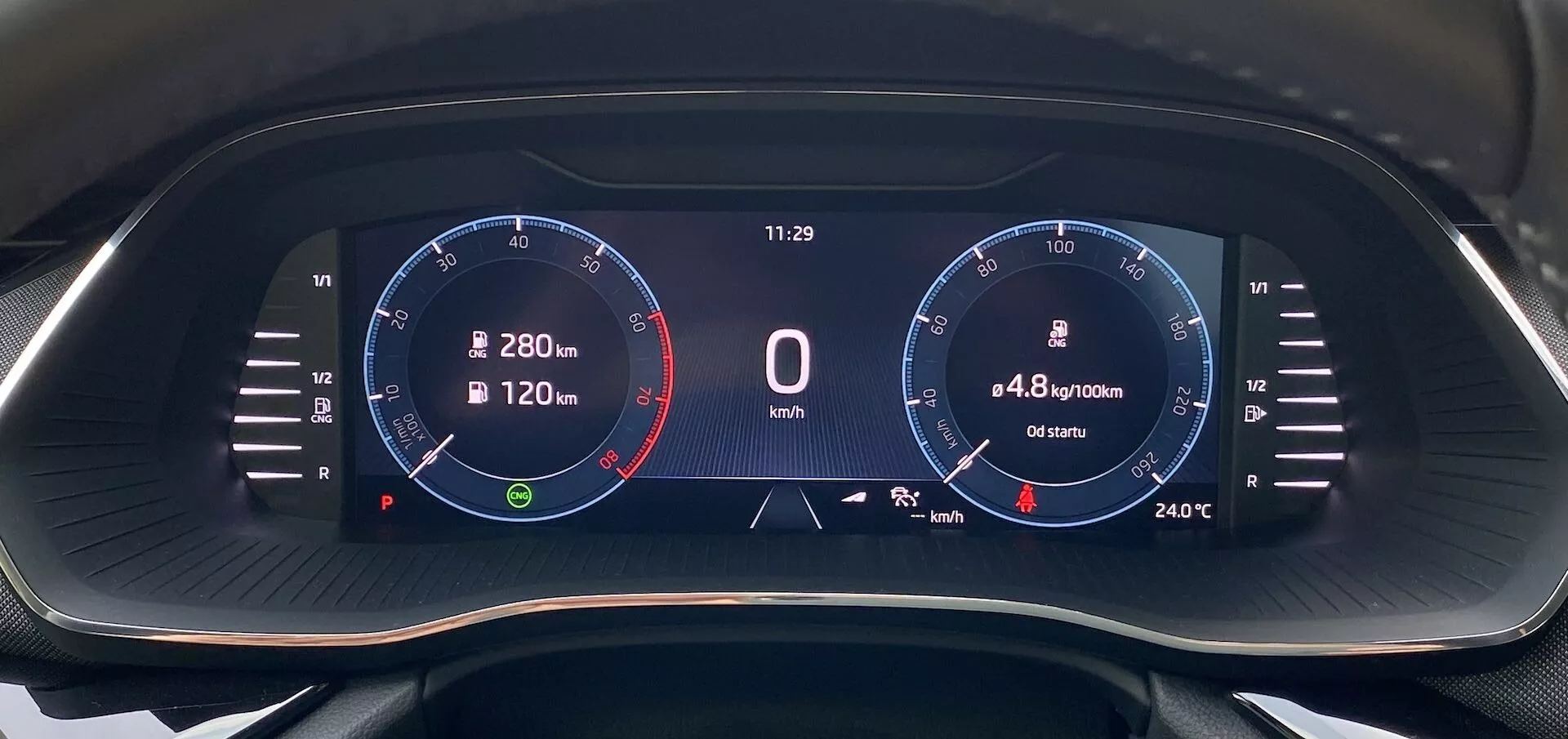 Close-up do painel de instrumentos digital do Skoda Octavia 2020 na perspectiva do motorista, apresentando uma tela widescreen com fundo preto e gráficos digitais vibrantes. Do lado esquerdo, um tacômetro com uma escala de até 8.000 RPM com linha vermelha a 6.500 RPM, agulha em repouso. No centro, um indicador de velocidade digital mostrando '0 km/h', um relógio digital marcando '11:29', consumo de combustível '4,8 l/100km' e uma distância de '6540 km'. No lado direito, um gráfico que se assemelha a um velocímetro com marcações até 280 km/h e leitura de temperatura '24°C'. Ícones incluem uma bússola de navegação e um indicador de nível de combustível.