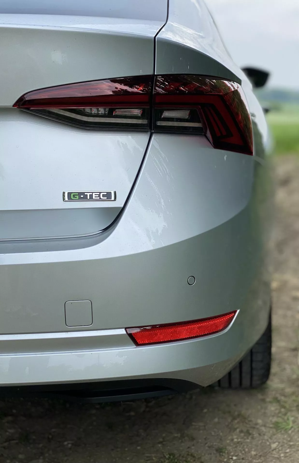 Vista oblíqua em close-up da seção traseira direita de um Skoda Octavia Limousine 2020 prateado. A imagem destaca a luz traseira, emblema G-TEC, design elegante do porta-malas, para-choque traseiro, refletor traseiro e acabamento de pintura metálica. O fundo desfocado realça o foco nas características de design do carro.