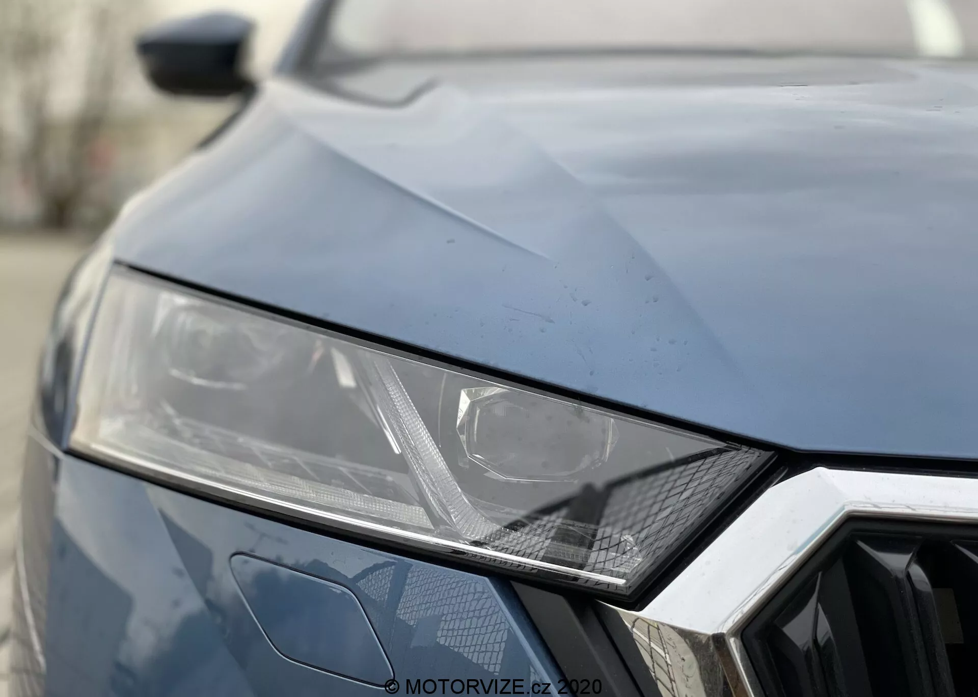 Vista de perto da parte frontal do Skoda Octavia 2020. Cor escura, mostrando o farol esquerdo com design angular elegante sugerindo tecnologia LED ou HID, padrão geométrico hexagonal da grade e vincos angulares no capô para uma aparência esportiva.