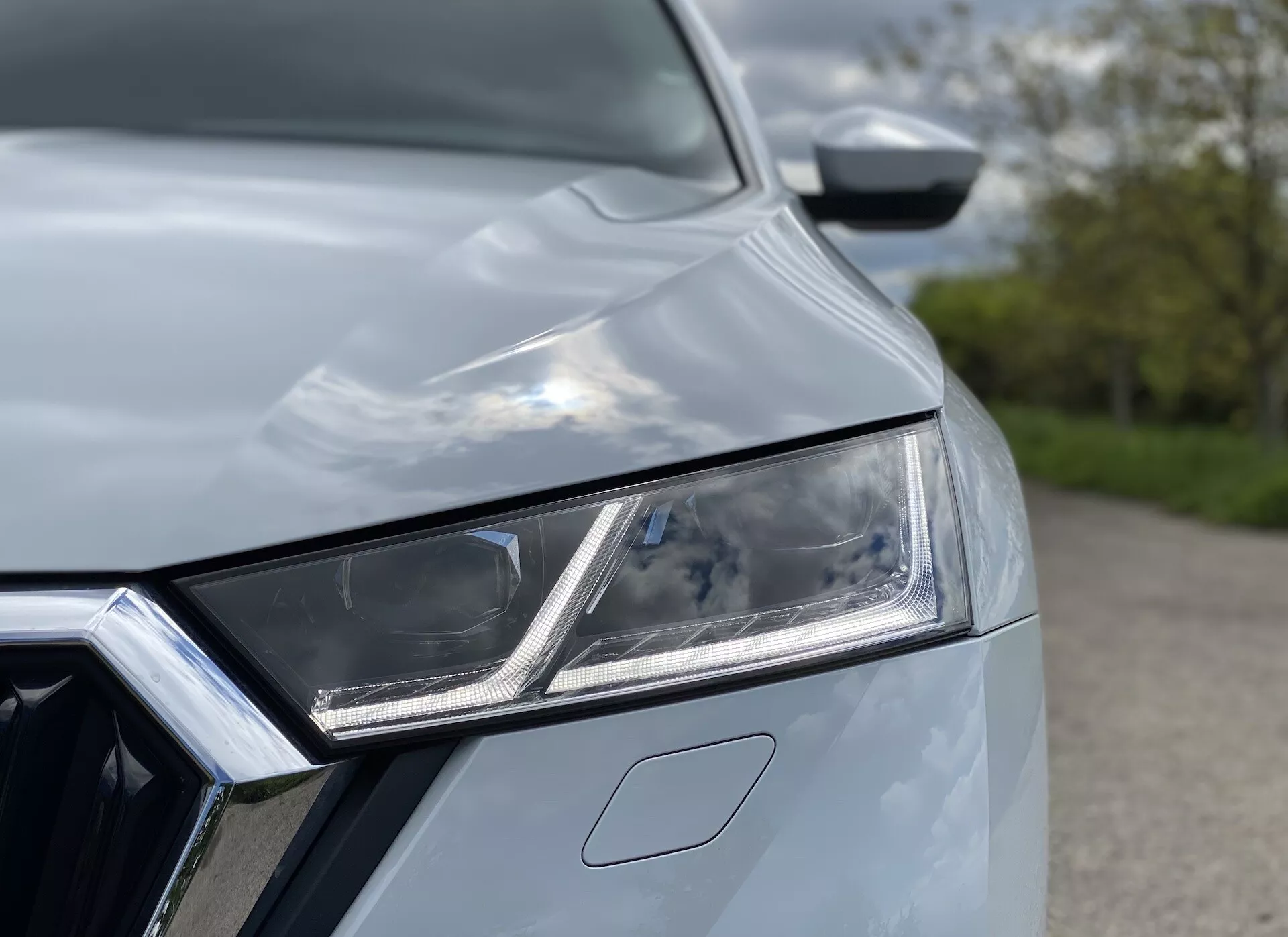 Vista aproximada do Skoda Octavia Limousine 2020, focando no intrincado conjunto de faróis dianteiros esquerdos com elementos de LED e luzes diurnas. Parte da grade frontal cromada é visível, junto com o capô do carro com curvas aerodinâmicas, criando uma aparência moderna e estilosa que indica tecnologia e design premium.