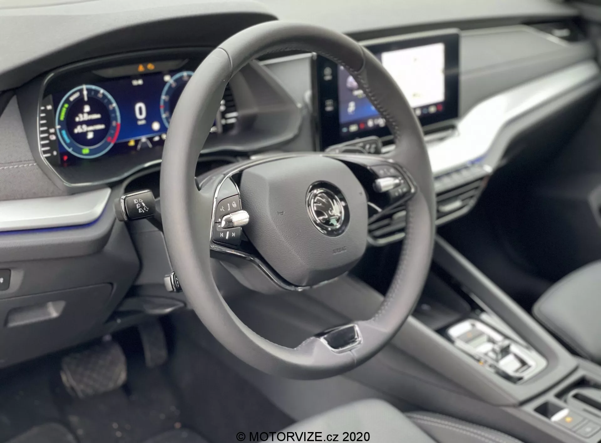 Interior do Skoda Octavia Limousine 2020 com foco na área do motorista a partir de um ângulo ligeiramente elevado, mostrando um volante moderno de três raios com botões multifuncionais, logotipo central do fabricante e painel de instrumentos totalmente digital exibindo 0 km/h. As características visíveis incluem uma grande tela sensível ao toque de infotainment, botões e botões minimalistas de controle climático, uma alavanca de câmbio que sugere transmissão automática, juntamente com volante revestido em couro, estofamento em couro e detalhes cromados para uma sensação premium