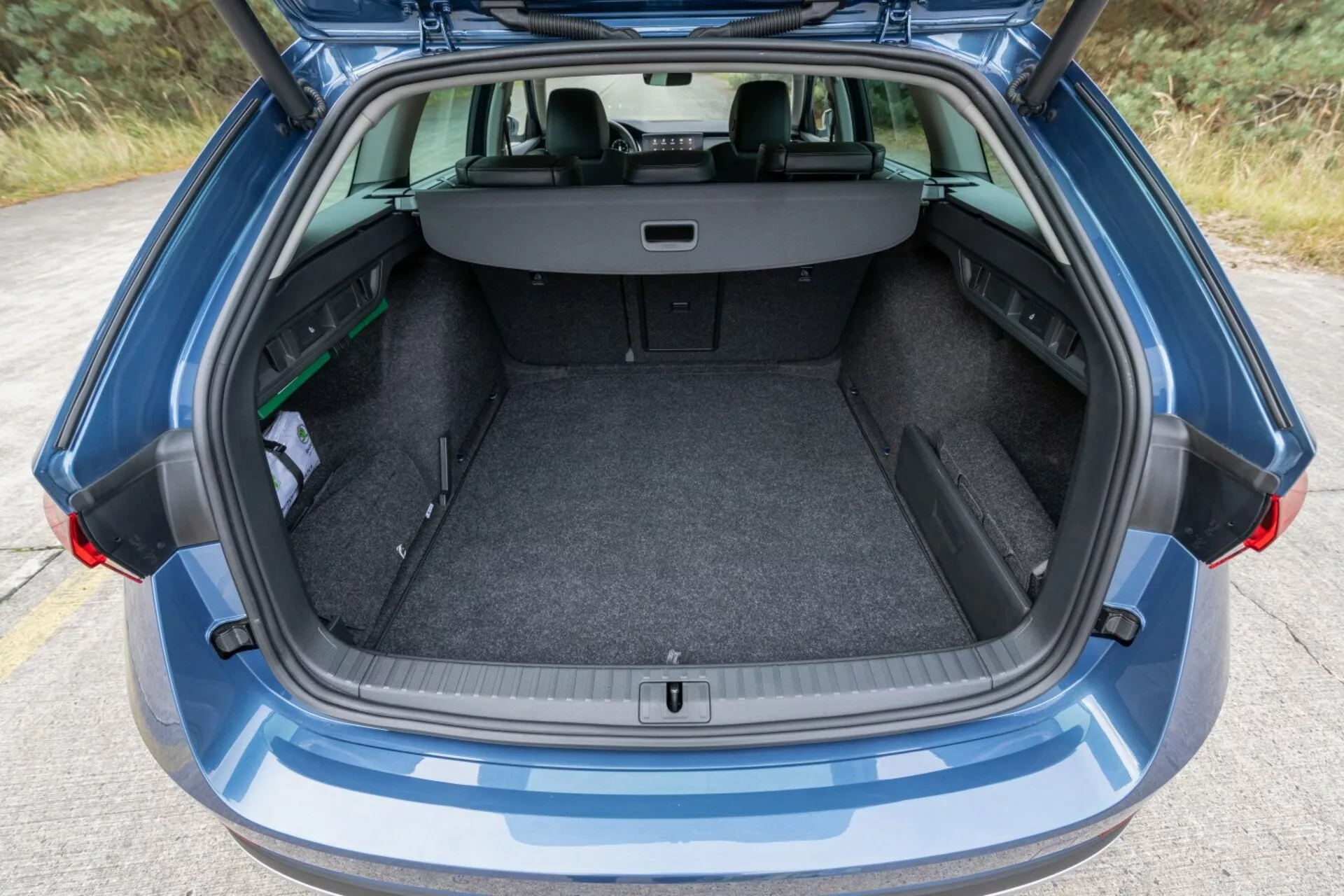Vista traseira de um Skoda Octavia Limousine 2017 destacando seu espaço de bagagem espaçoso e limpo com porta-malas aberto, cobertura de carga retrátil e assentos traseiros visíveis em configuração dividida 60/40 para maior capacidade de carga, ao lado de um pequeno guarda-chuva e um objeto verde, sob luz ambiente.