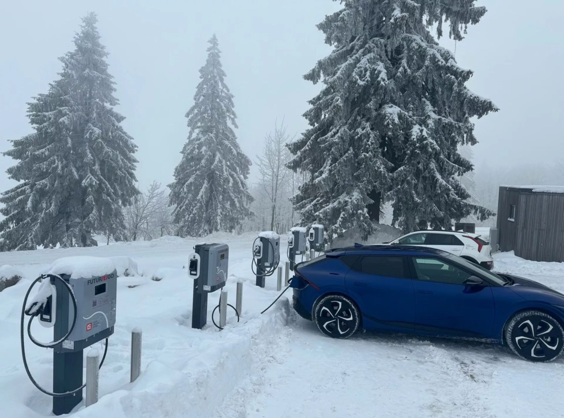 Limousine Skoda Octavia 2020 azul carregando em uma estação de veículos elétricos, vista diagonalmente do lado traseiro, destacando suas rodas de liga leve, porta de carregamento e design preparado para o inverno em condições de neve.