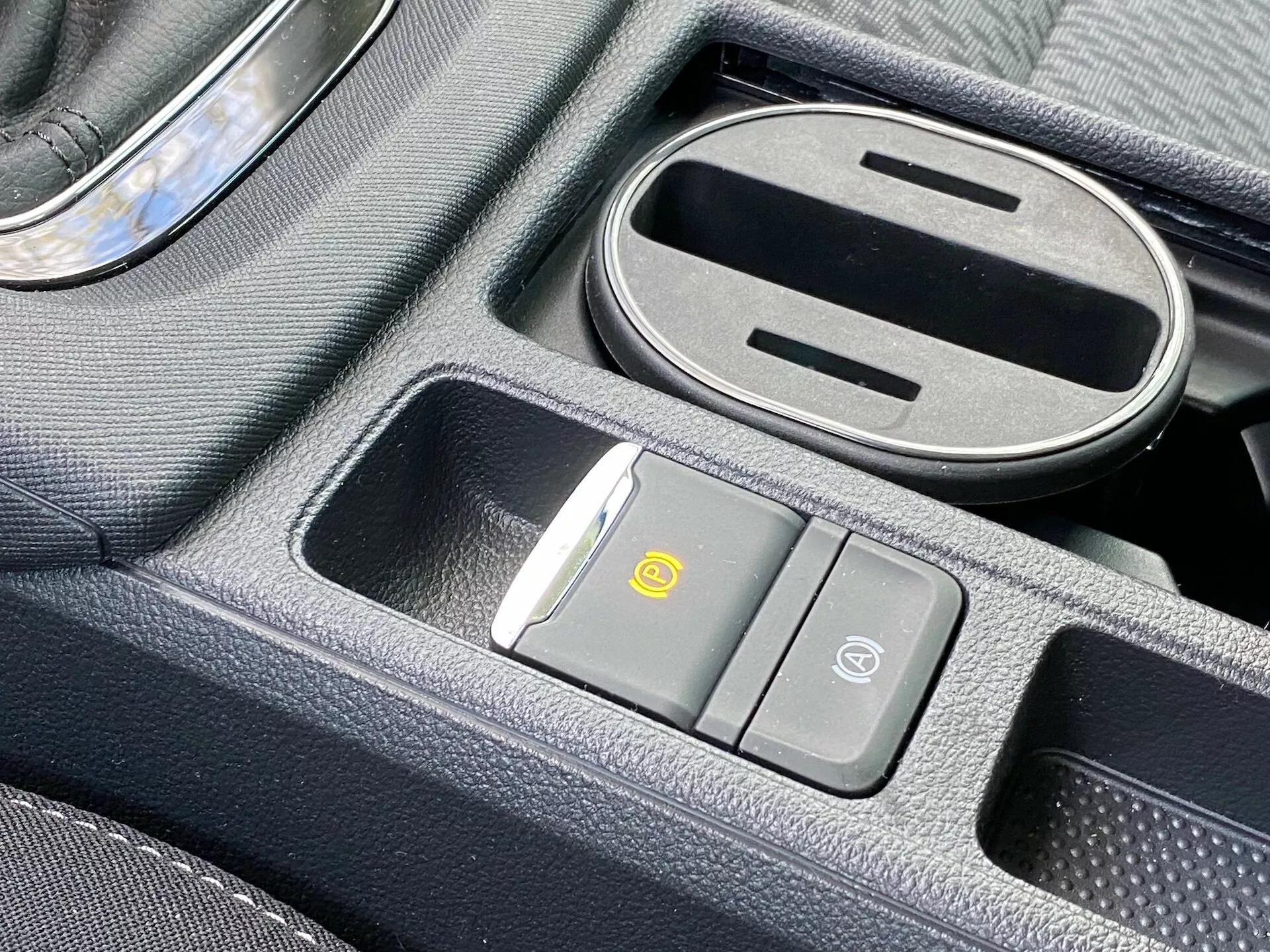 Close-up do console central do Škoda Octavia 2020 com almofada de carregamento sem fios, botão de controle de circulação de ar, botão de segurança do veículo, compartimento de armazenamento parcialmente aberto com forro de borracha e alavanca de câmbio com detalhe cromado.