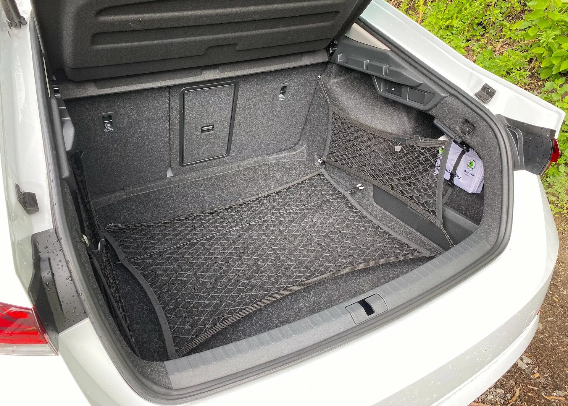 Vista traseira do espaço de carga aberto de um Škoda Octavia 2020 (octavia-limousine) com uma superfície acarpetada e acessório de rede de carga para armazenamento seguro. As características incluem revestimento de plástico para proteção, vários ganchos e pontos de fixação para opções adicionais de carga. Um pequeno compartimento embutido à direita com uma tampa indica armazenamento adicional ou acesso a ferramentas essenciais.