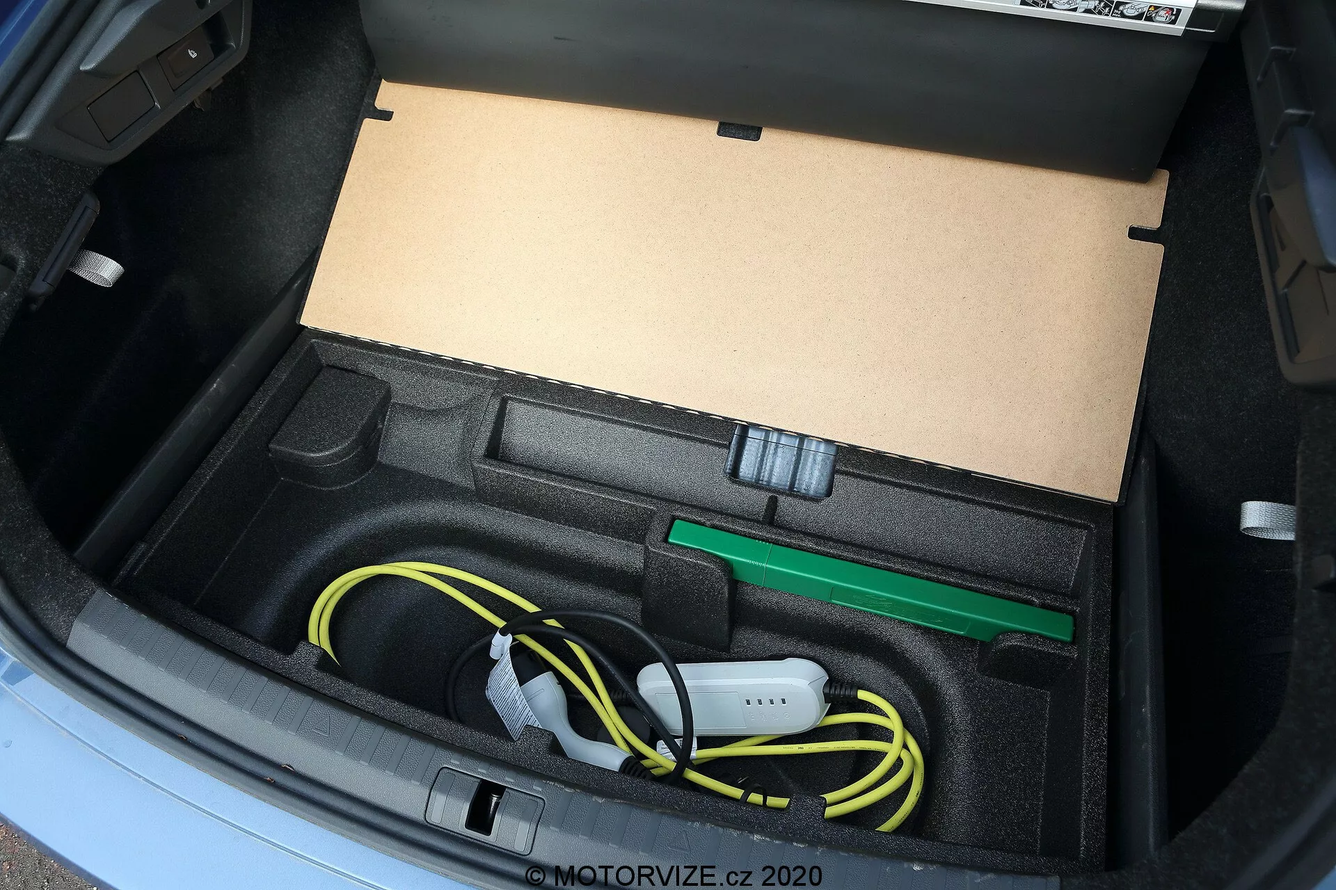 Vista de close-up do porta-malas do Skoda Octavia 2020, mostrando um compartimento sob medida projetado para armazenar o cabo de carregamento do veículo elétrico e acessórios, incluindo um cabo de carregamento amarelo enrolado e um gancho de reboque verde, capturado de um ângulo alto com iluminação natural.