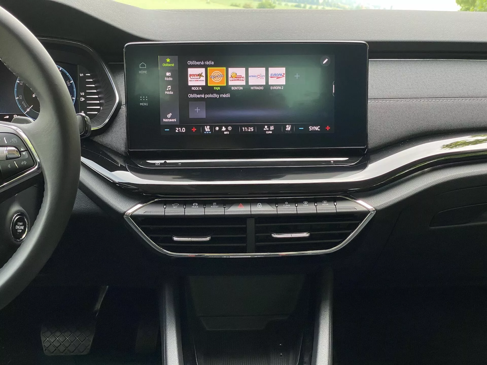 Interior do Škoda Octavia 2020 limousine, destacando a consola central e o sistema de infotainment a partir da perspectiva do banco da frente. O grande ecrã táctil em orientação paisagem exibe uma interface de utilizador colorida com ícones para navegação, reprodução de mídia e configurações do veículo. Abaixo do ecrã táctil, encontram-se saídas de ar fluídas com acabamento cromado, seguidas de botões físicos e controlos para o sistema de climatização. O painel de instrumentos e a consola apresentam uma mistura de texturas semelhantes a couro e plásticos mate e brilhantes, sugerindo um design de alta qualidade para o segmento de mercado médio a superior.
