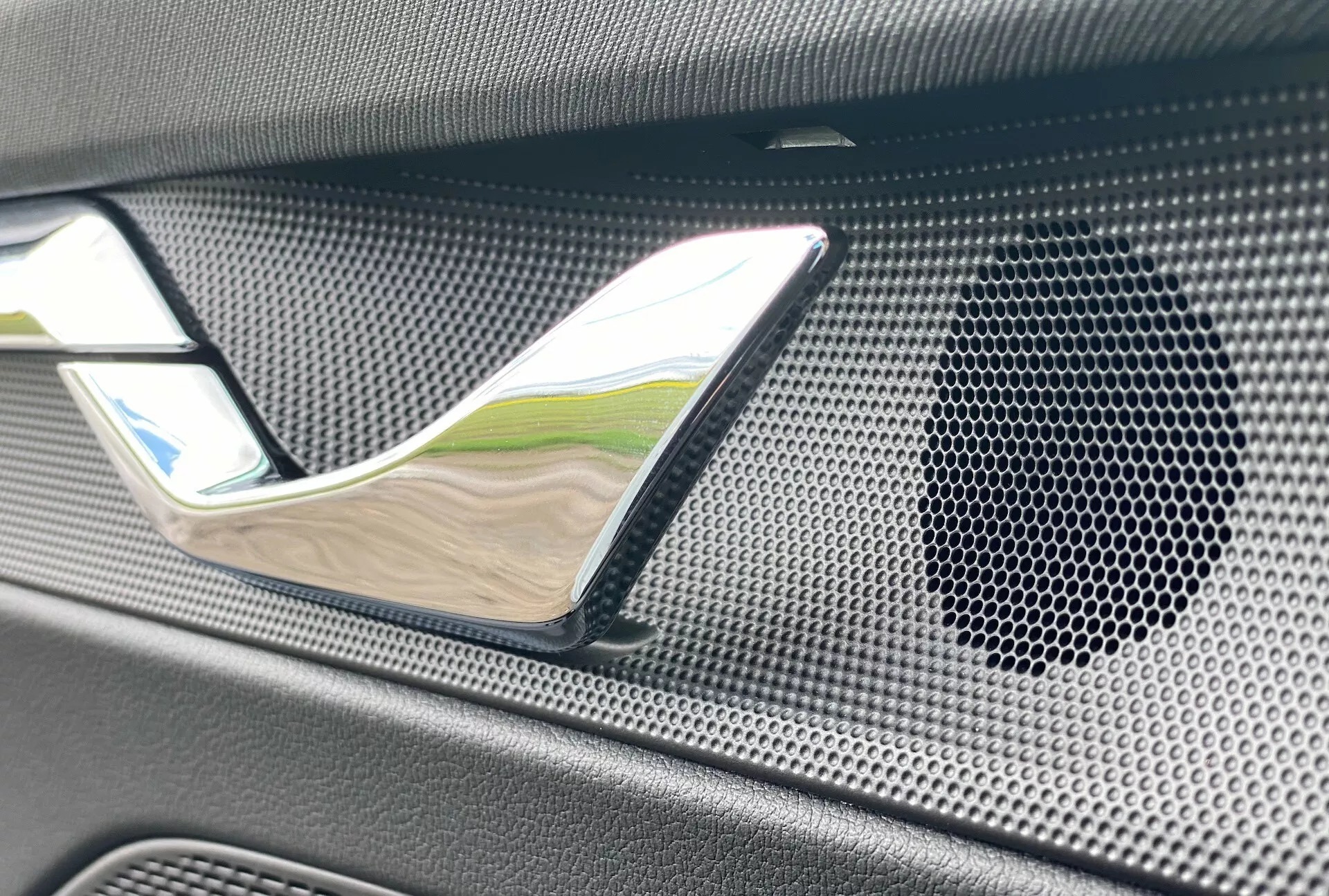 Foto de detalhe interior do Skoda Octavia limousine 2020, destacando a maçaneta da porta com acabamento cromado e a grade do alto-falante com padrão de colmeia em material texturizado, possivelmente de fibra de carbono, enfatizando luxo e sistema de áudio de alta fidelidade.