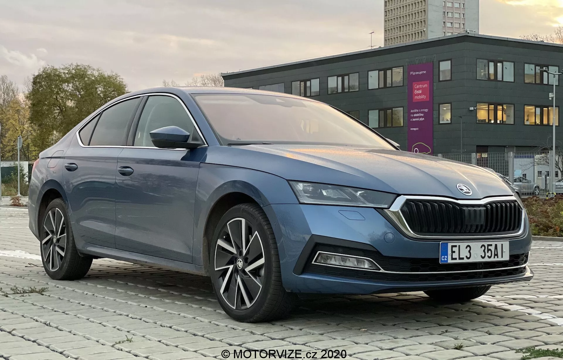 Foto profissional do modelo de quatro portas Skoda Octavia Limousine 2020 tirada em um ângulo de três quartos da frente esquerda, mostrando claramente a grade distinta, faróis LED elegantes, para-choque dianteiro com possíveis luzes de neblina, linhas suaves da carroceria, rodas de liga leve multiraio, retrovisores com sinais de direção integrados e acabamento premium em cromo das janelas em um ambiente urbano ou suburbano ao amanhecer ou anoitecer.