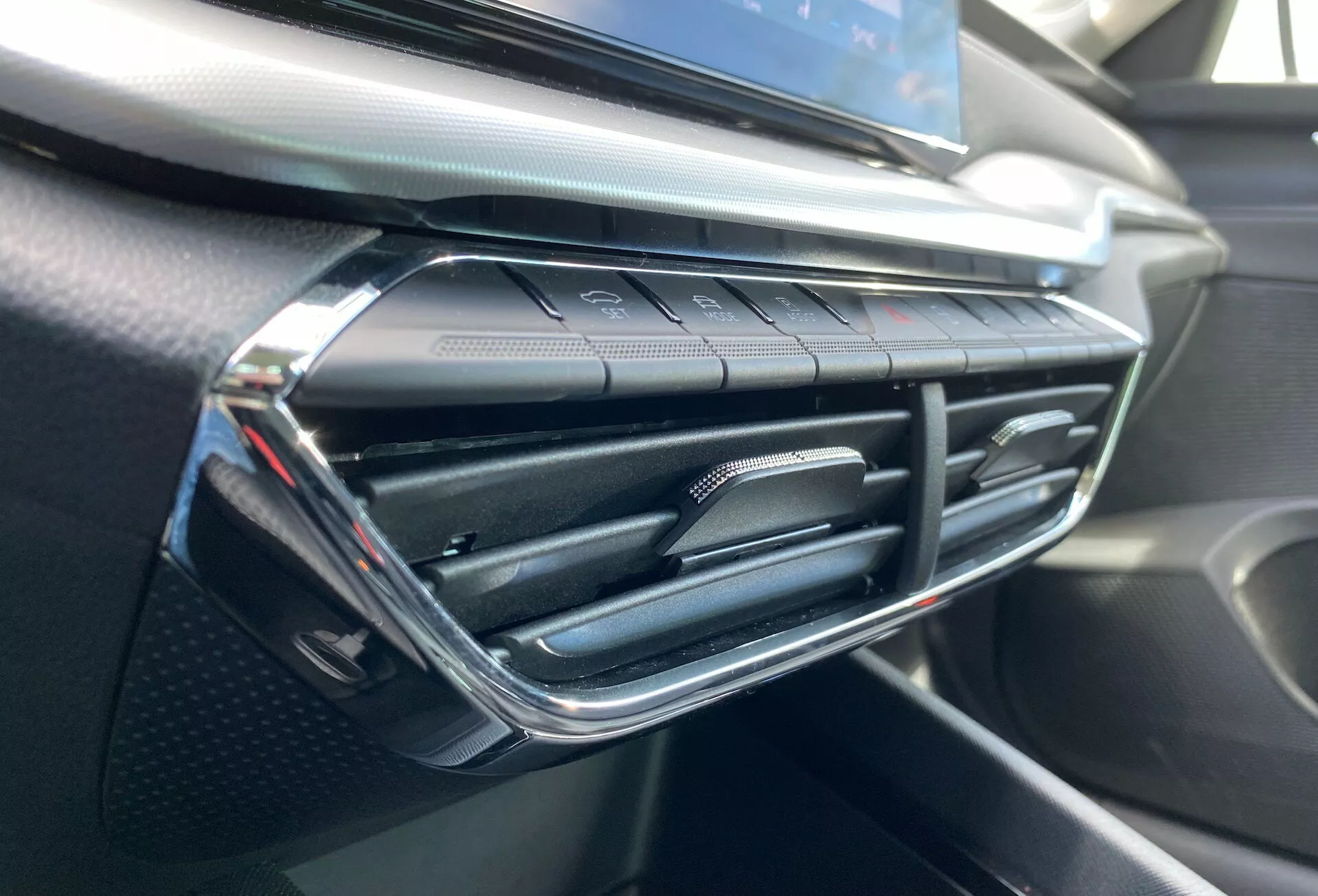 Vista aproximada do interior do Skoda Octavia 2020 destacando a saída de ar-condicionado e a área circundante do painel, com um design moderno da ventilação com toques de cromo e botões sensíveis ao toque para controle de clima abaixo, em um painel texturizado e semelhante à fibra de carbono.