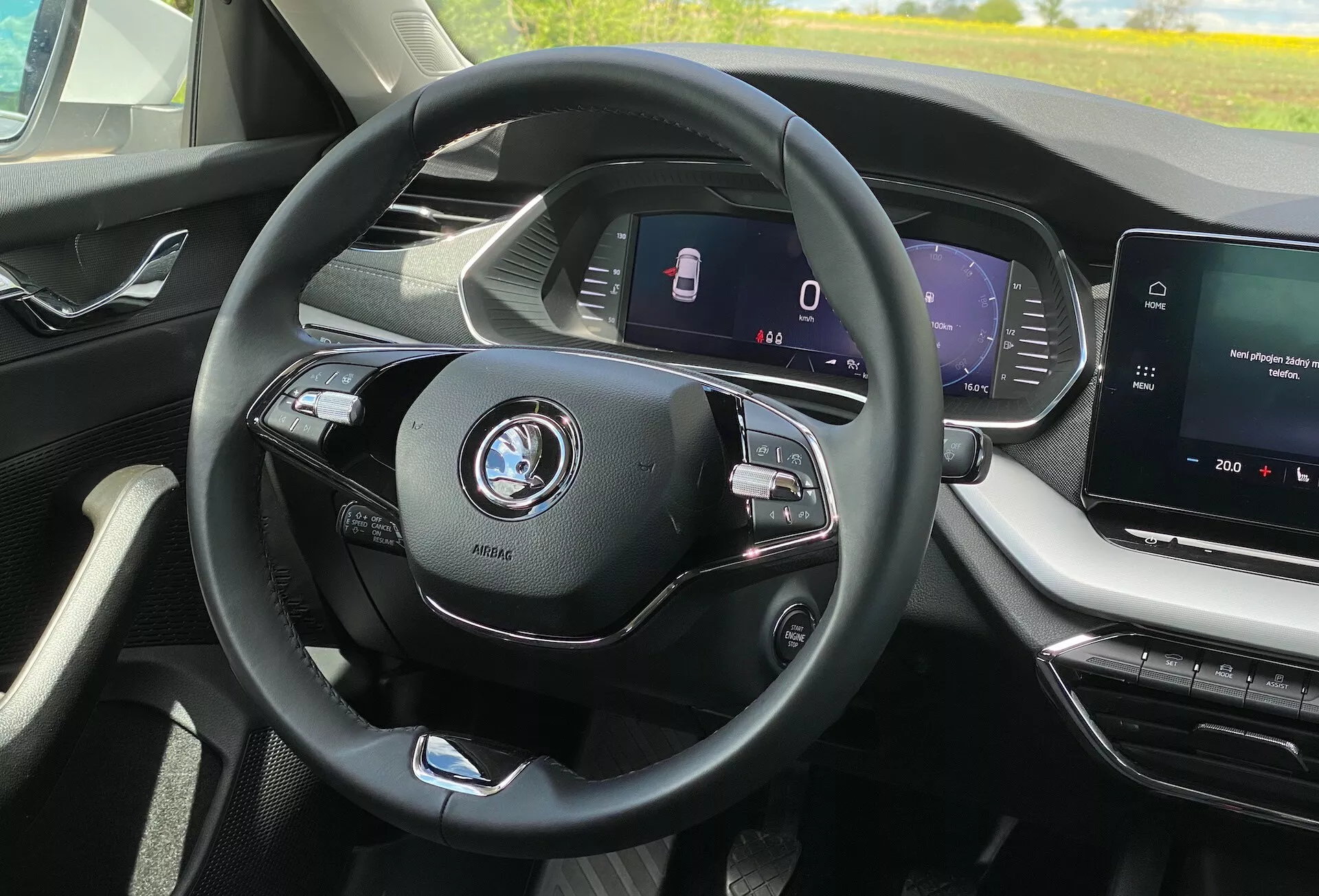 Vista interna do Skoda Octavia 2020 a partir da perspectiva do assento do motorista; volante moderno de três raios centrado com controles multifuncionais para mídia e telefone, emblema do carro visível; painel de instrumentos totalmente digital exibindo velocidade e recursos de segurança como assistência para manutenção de faixa; console central com tela sensível ao toque de infotainment, mostrando sistema de mídia e possível navegação; interior moderno e sofisticado com linhas limpas e saídas de ar bem desenhadas; sem visão do exterior, apenas o ambiente imediato do motorista na cabine; indícios de tecnologia automotiva avançada como controle de cruzeiro adaptativo e recursos de conectividade.