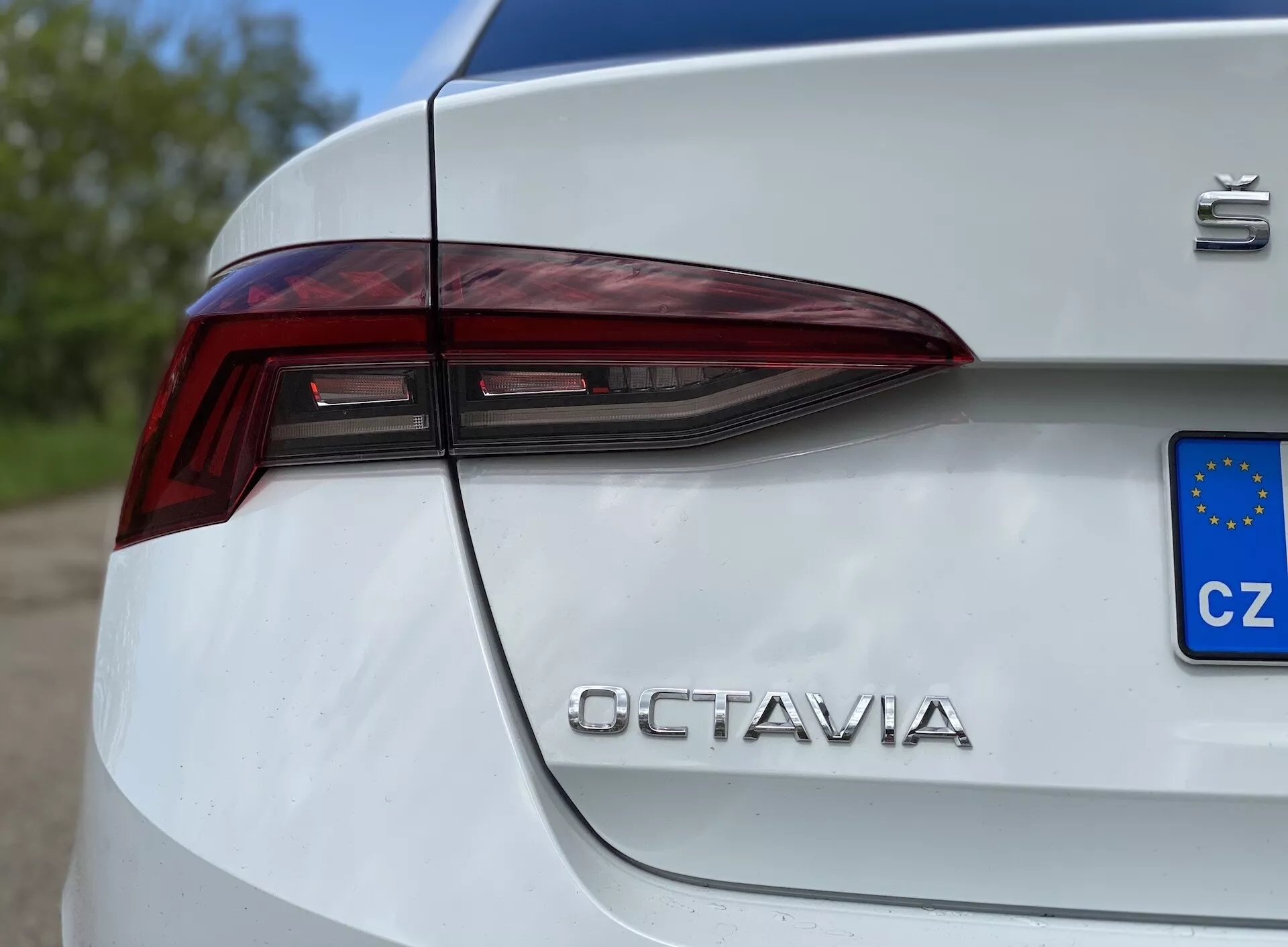 Vista lateral em close-up do quarto traseiro de um Škoda Octavia Limousine branco de 2020, destacando o design angular das luzes traseiras LED que se estende para a tampa do porta-malas, junto com o emblema 'Škoda' e as letras cromadas 'OCTAVIA', com uma placa europeia (CZ) parcialmente visível, capturada de um ângulo baixo.