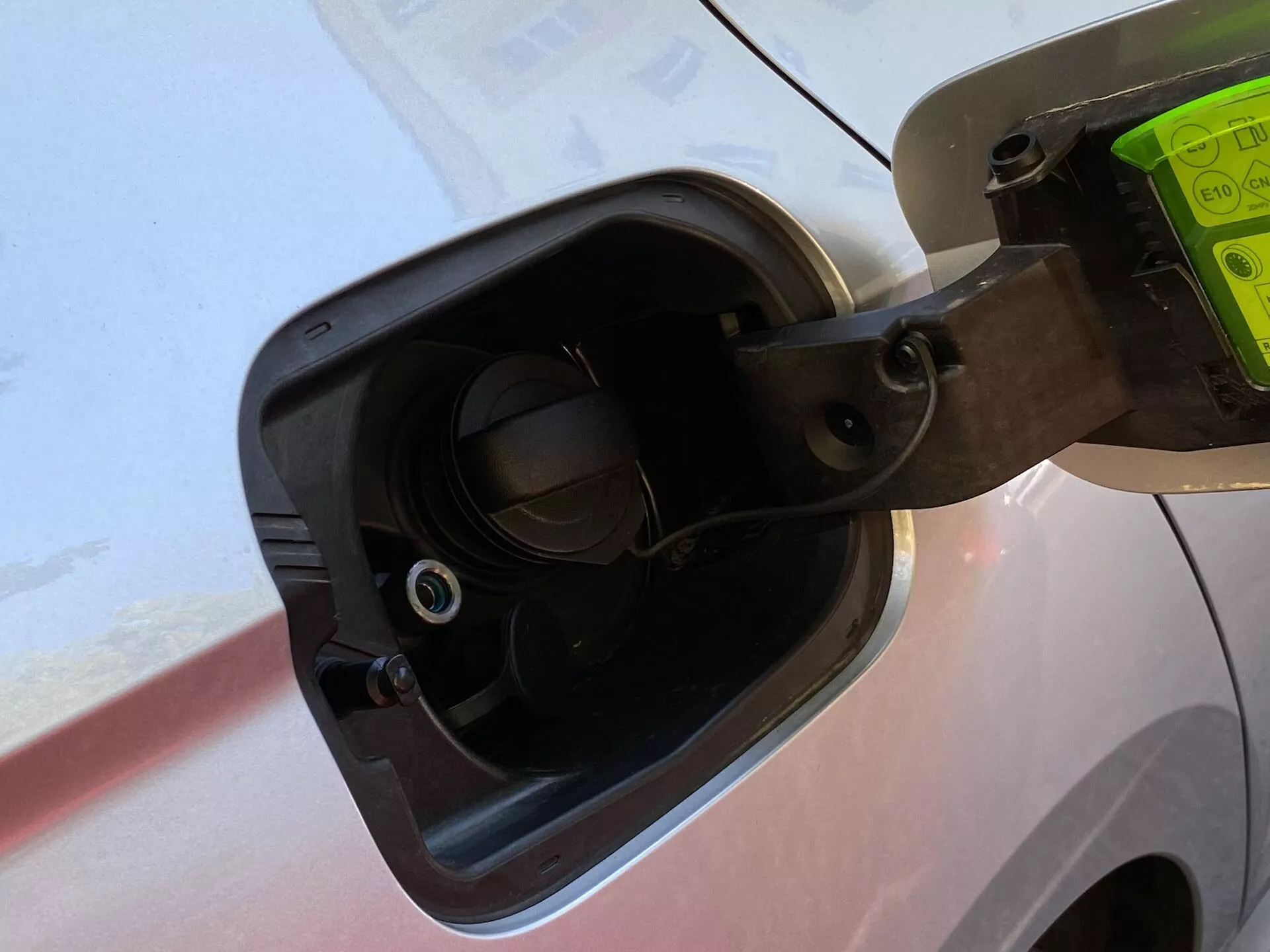 Close-up da área de abastecimento de combustível de um Skoda Octavia Limousine 2020, mostrando a tampa de combustível aberta presa por uma correia flexível, os detalhes circundantes da carroceria do veículo e o bocal de abastecimento de combustível embutido com uma válvula visível, tudo visto de um leve ângulo para baixo.