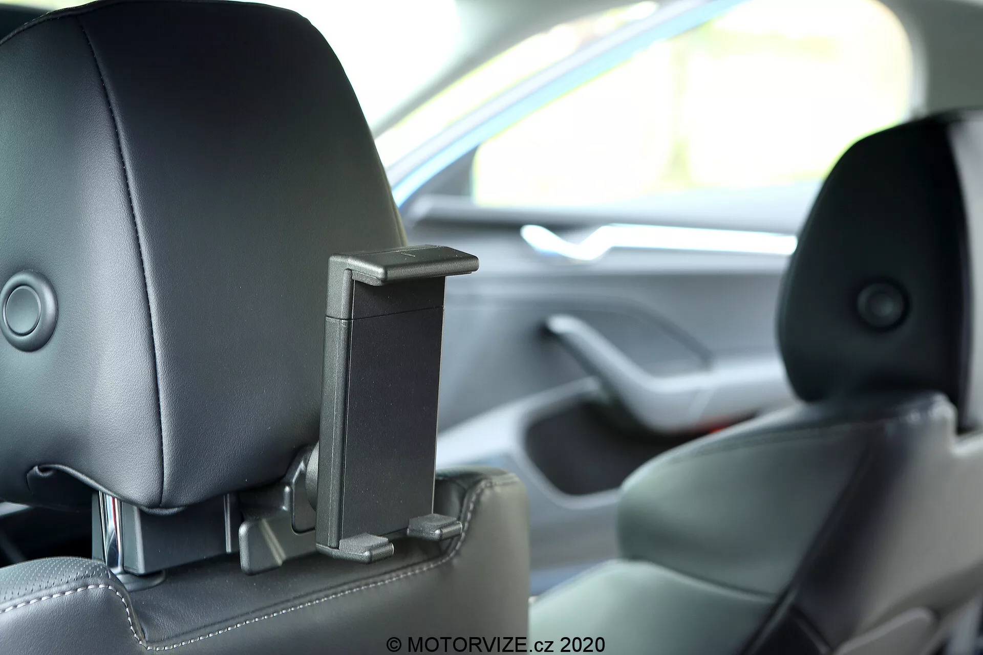 Vista interior de um Skoda Octavia 2020 mostrando o encosto de cabeça traseiro central com um componente retrátil integrado, possivelmente uma característica de entretenimento ou segurança. A imagem captura o encosto de cabeça da perspectiva de um passageiro traseiro à altura dos olhos com pouca profundidade de campo, mostrando estofamento de couro bicolor e destacando o design tecnológico e ergonômico avançado.